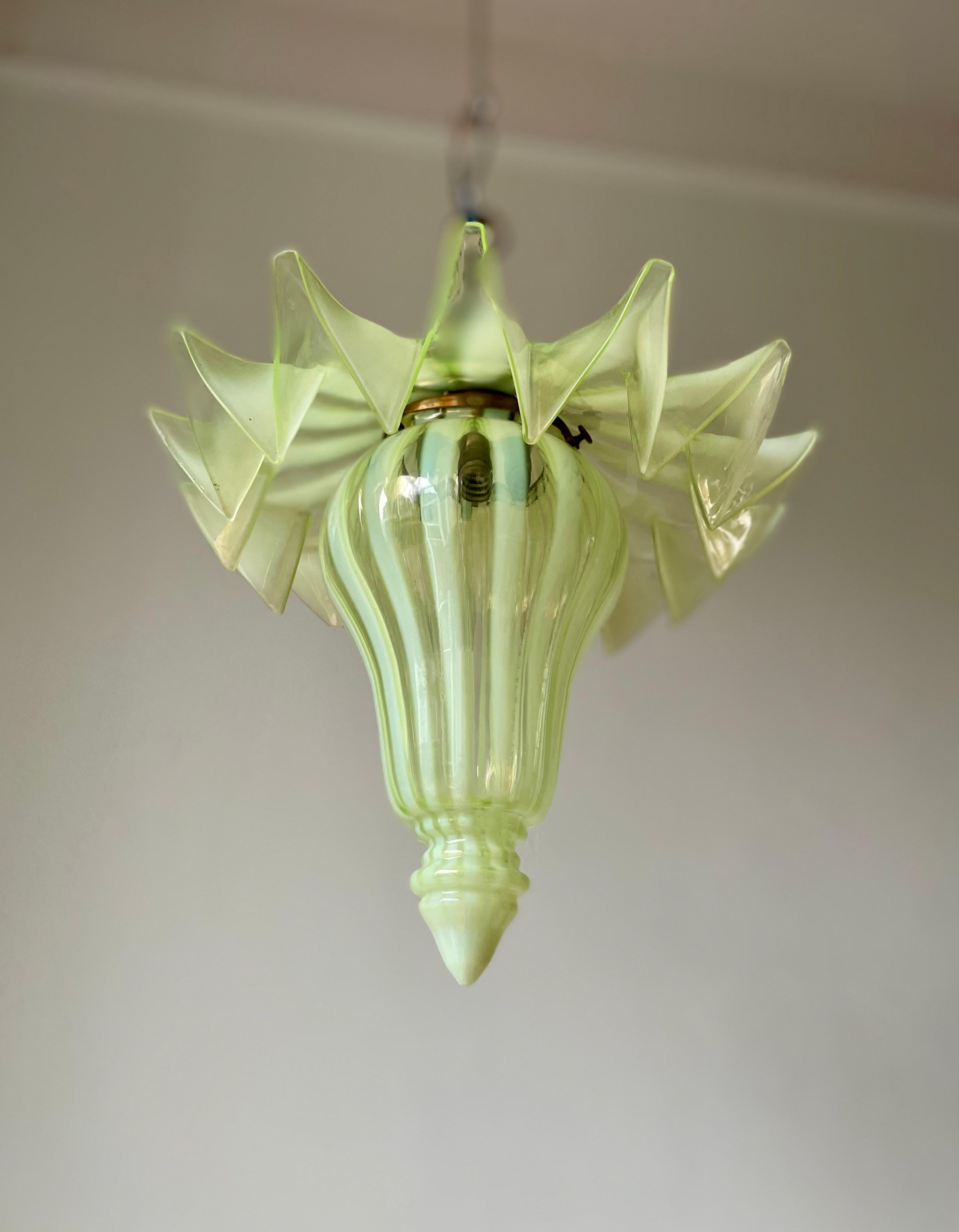 Remarkable antique mouthblown art glass pendant likely manufactured in France in the early 20th century.  Clear and light lime yellow stripes on broad flowing skirt placed over soft curved elongated base with pointed tip. Brass mount with small