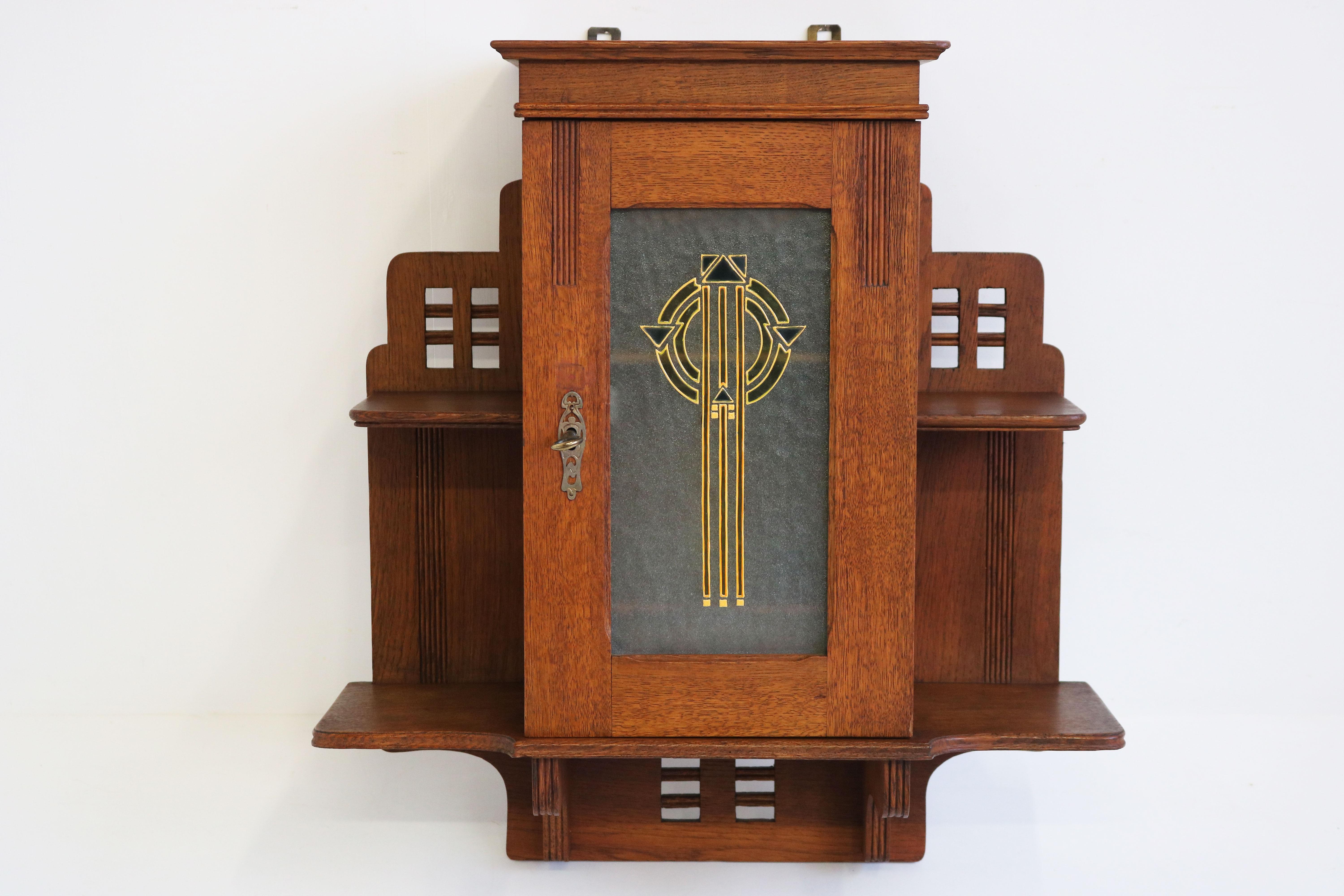 Breathtaking & exceptional! This antique French Art Deco wall cabinet 1920 with geometric enamel glass artwork.
Made out of solid carved European oak with amazing enamel glass art piece in Art Deco geometric shape. 
Interior has 1 shelf and 2