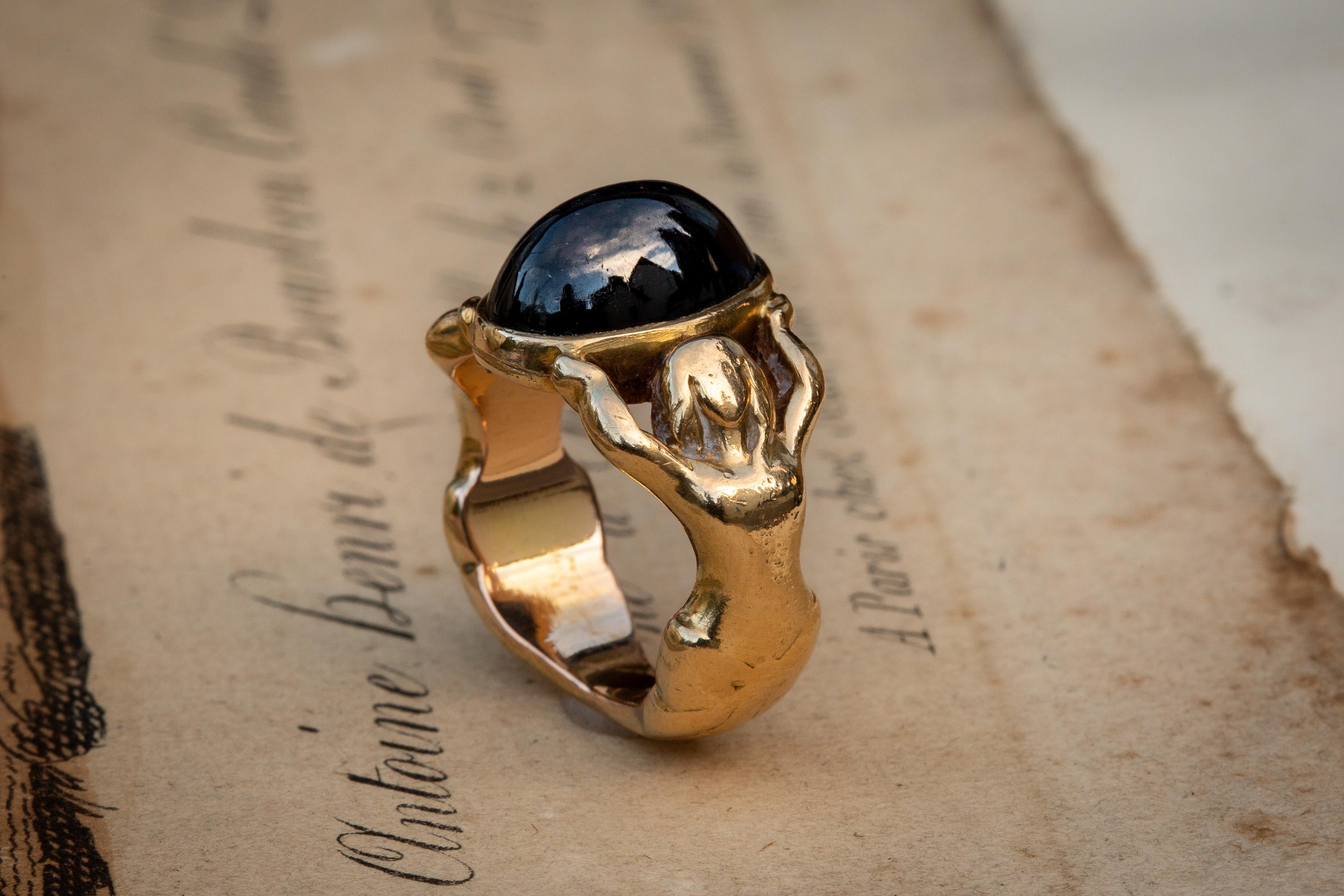 A superb French Art Nouveau figural statement ring, circa 1900. The mount is crafted in 18K yellow gold and features two nude outstretched ethereal ladies/nymphs who carry a stunning high-domed deep blue 8.87Ct sapphire cabochon. 

This highly