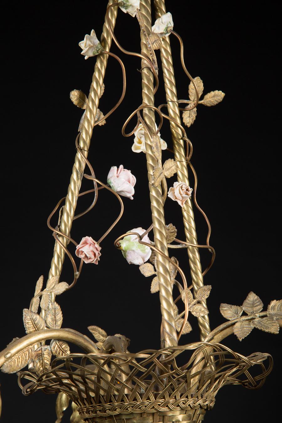 This French Belle Epoque woven basket chandelier is made of bronze and dates back to the late 19th century. Uniquely, and impressively, outside of the porcelain flowers, the entirety of the piece is made of bronze, including the woven basket. The