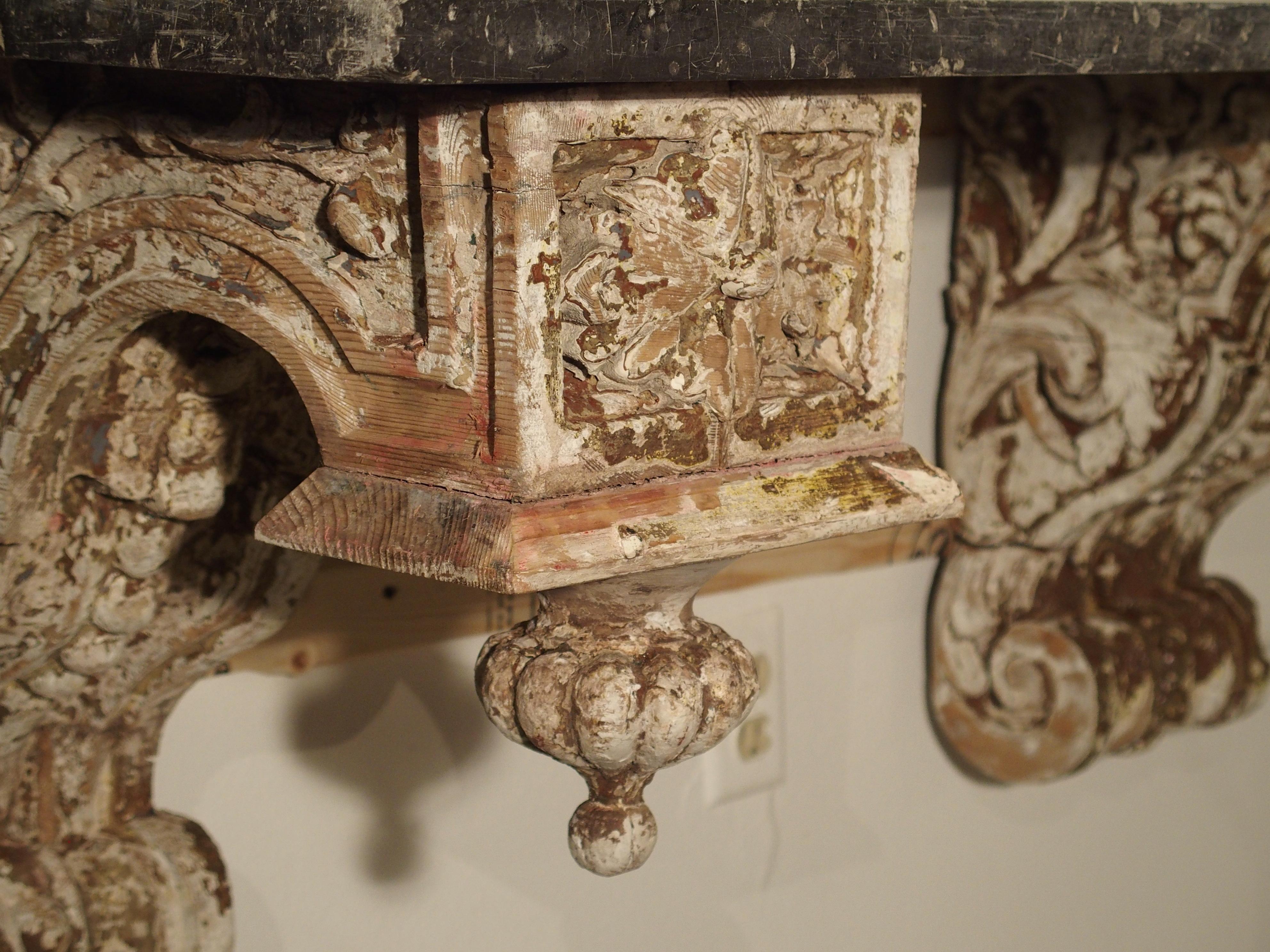 From France, this console table is comprised of two beautiful parcel painted 19th century brackets, and a rectangular black marble top. Each bracket is deeply carved with motifs of floral and foliate design. C and S-scrolls form the shapes of both.