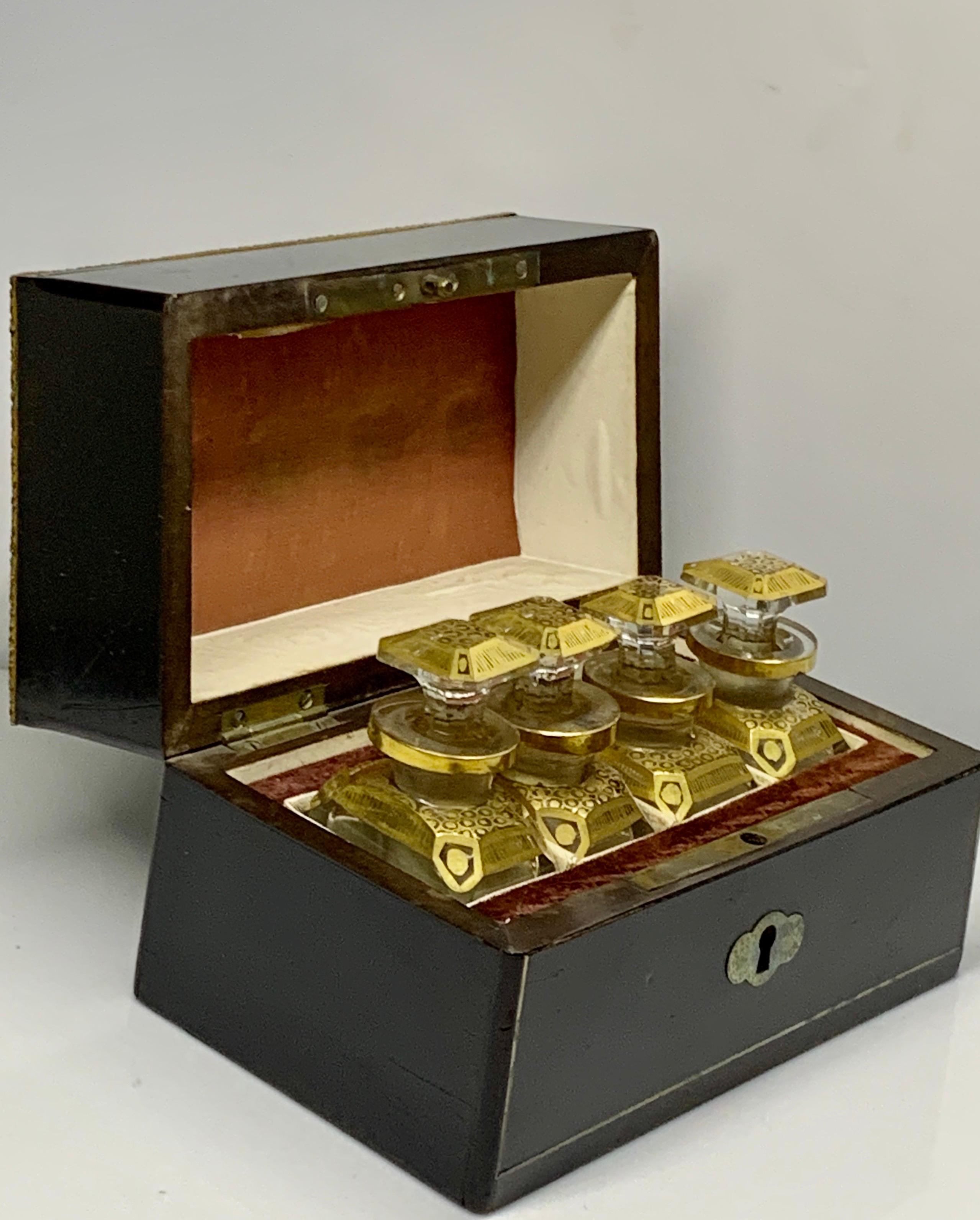 A late 19th century French ebonised and brass inlaid scent bottle casket Of shaped rectangular outline, the hinged lid concealing four gilt decorated clear glass bottles and stoppers, 6 inches (15 cm) wide by 3 1/2 inches (9 cm) High by 3 1/2 inches