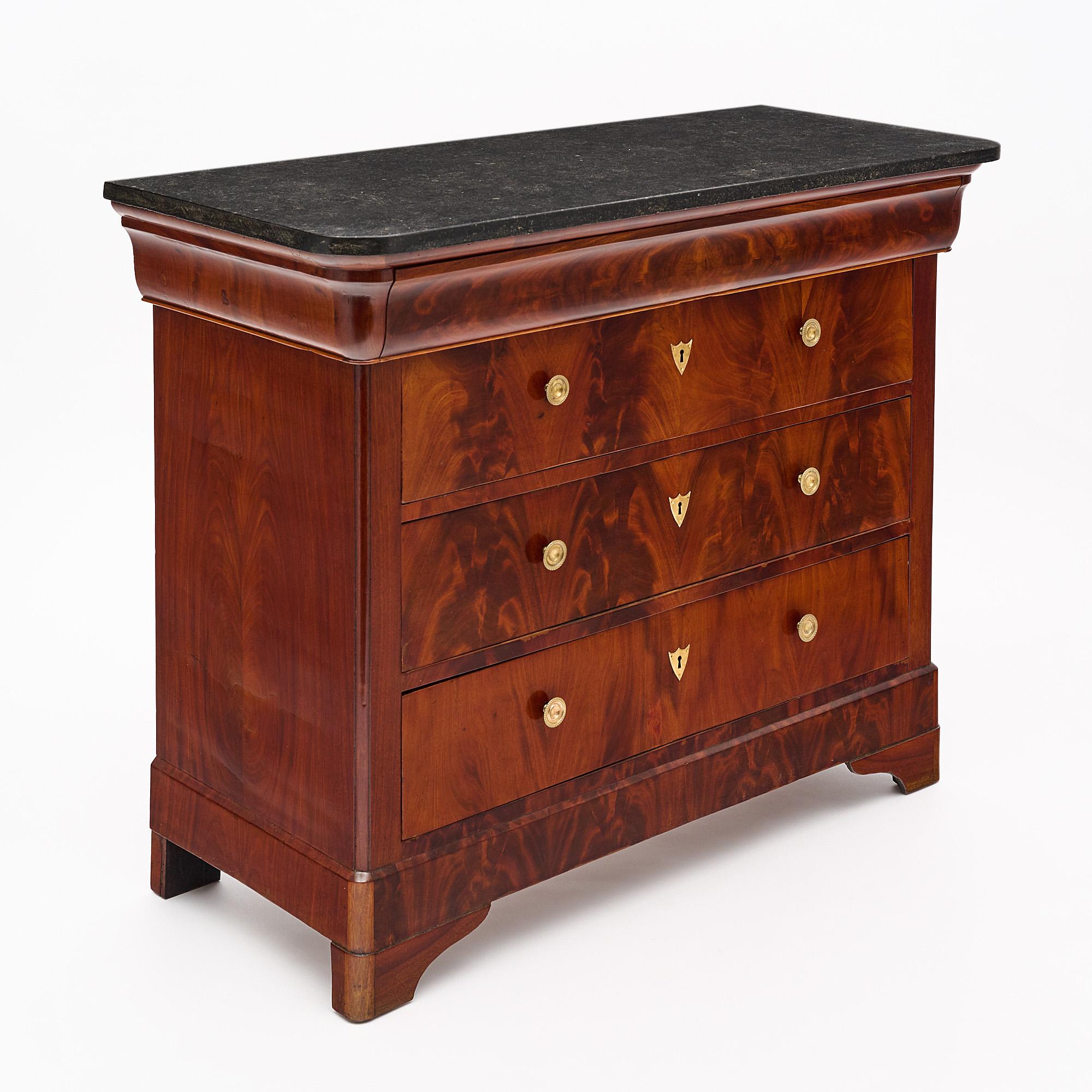 Chest of drawers, French, made of Cuban flamed mahogany. This piece has four dovetailed drawers with bronze wax cast pulls. The commode features an intact black marble slab top.