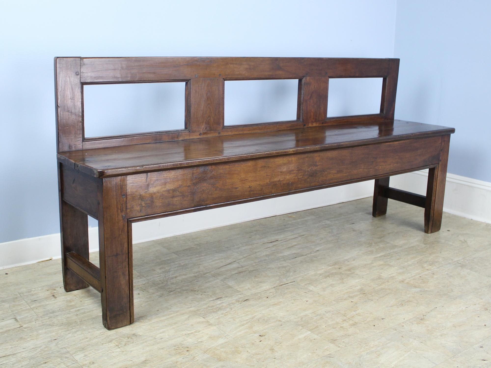 A solid handsome and sturdy chestnut bench with good depth and seat height. The wood glows with good color and patina. A simple silhouette to complement any decor. This would be right at the end of a bed or in a well appointed hall or mudroom.