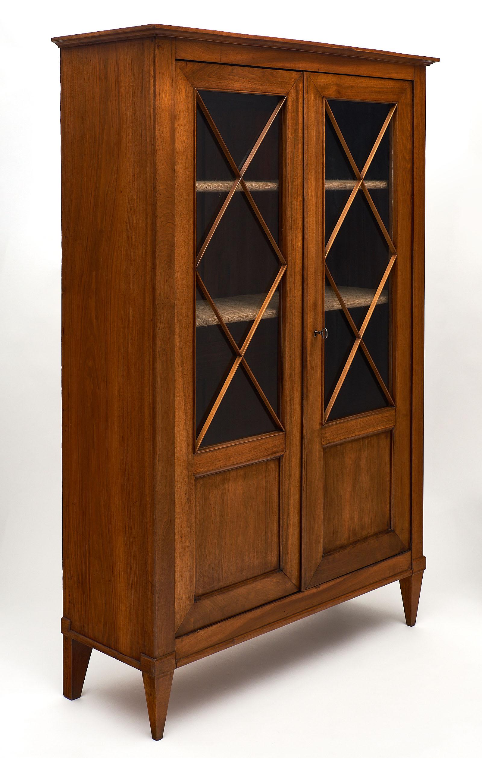 Elegant Directoire style French antique bookcase made of patinated cherrywood. We love the glass doors and interior shelving. The lock and key are in working condition and original to the piece.