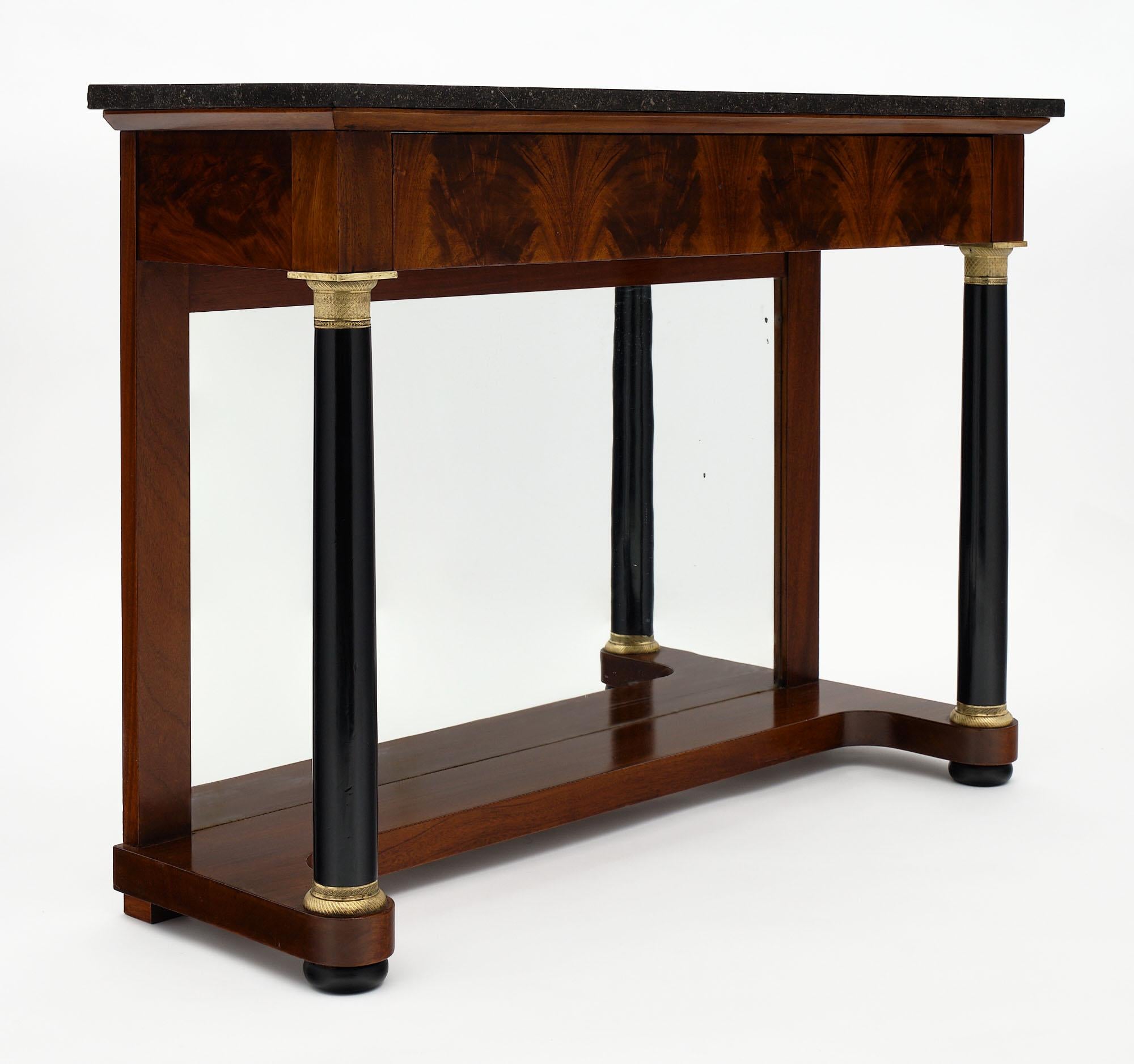 French antique Empire console table made of Cuban flamed mahogany and topped with a black marble slab. This elegant piece features a single drawer richly veneered and ebonized column legs with finely cast bronze ring ornamentation. There is also a
