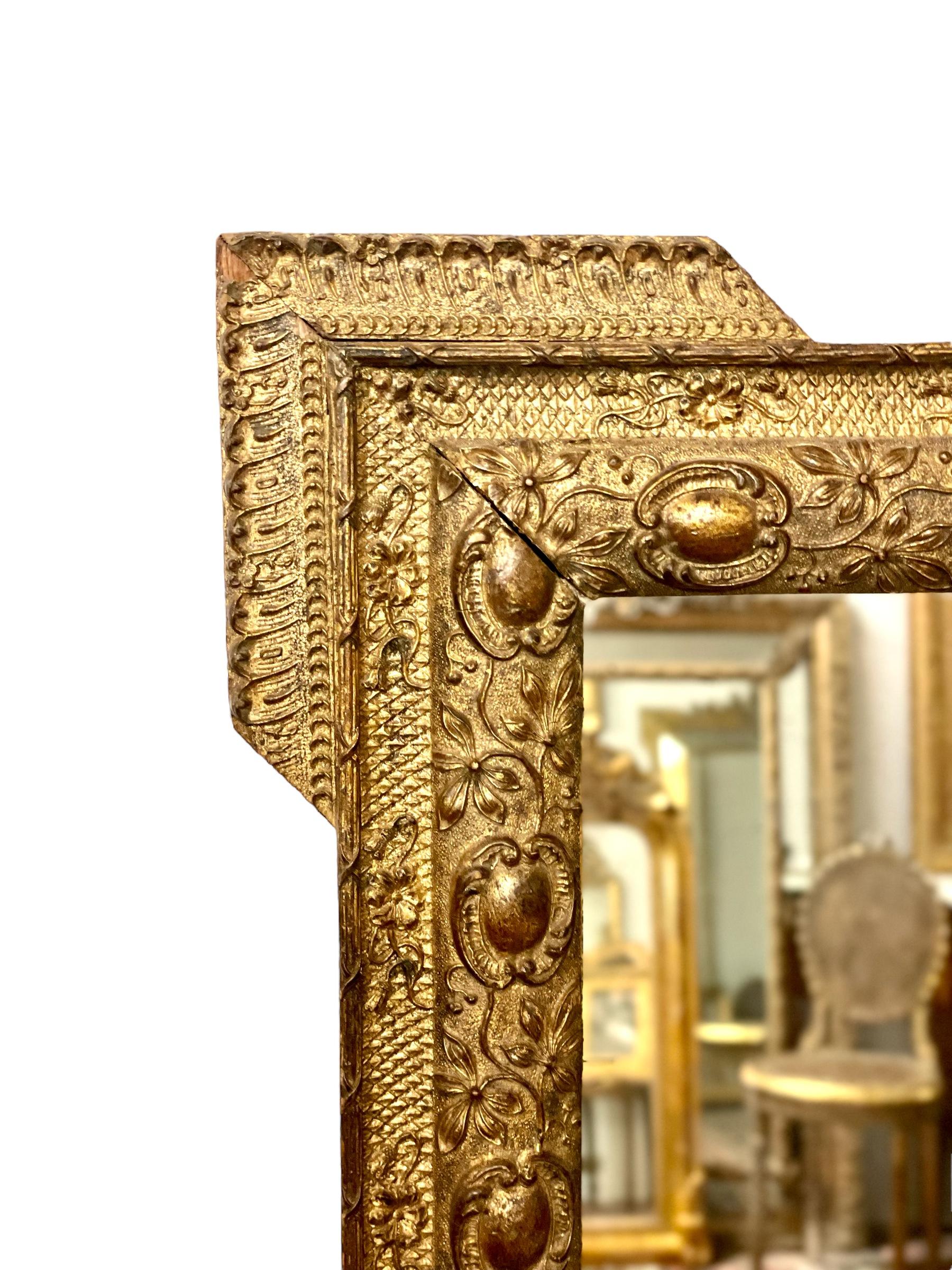 An intricately carved and very ornate wall mirror in wood and gilded stucco, decorated with oves and intertwined flowers against a background of stylised scales. Each corner features the addition of an elaborately carved 'step', which contributes