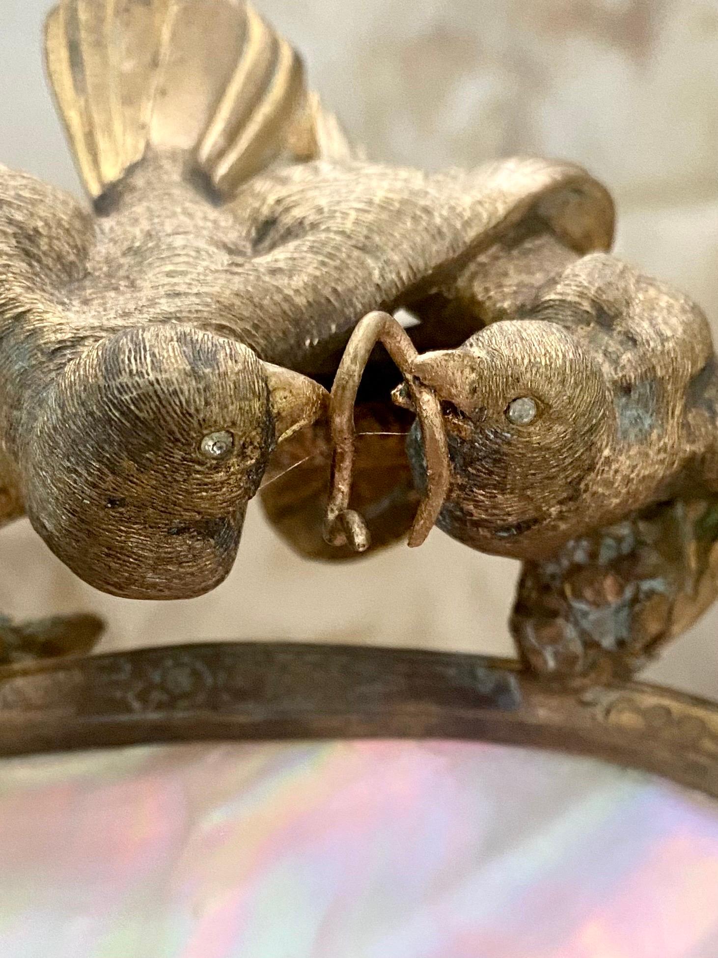 Intricate French gilt bronze work depicting lovebirds sharing a worm above a pearl egg nest upon a tree, while a cobra nestles at the tree base. The work is sublime and the jeweled eyes are exquisite details on this piece. It is beautiful from every