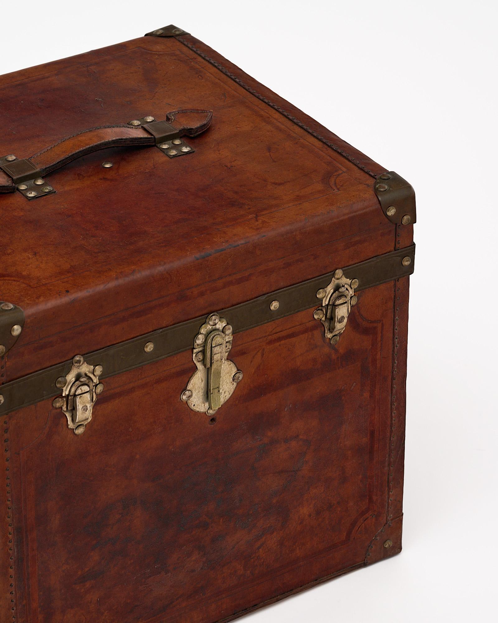 Traveling trunk, French, made with a patinated leather. This piece features three brass locks and beautiful detailing.