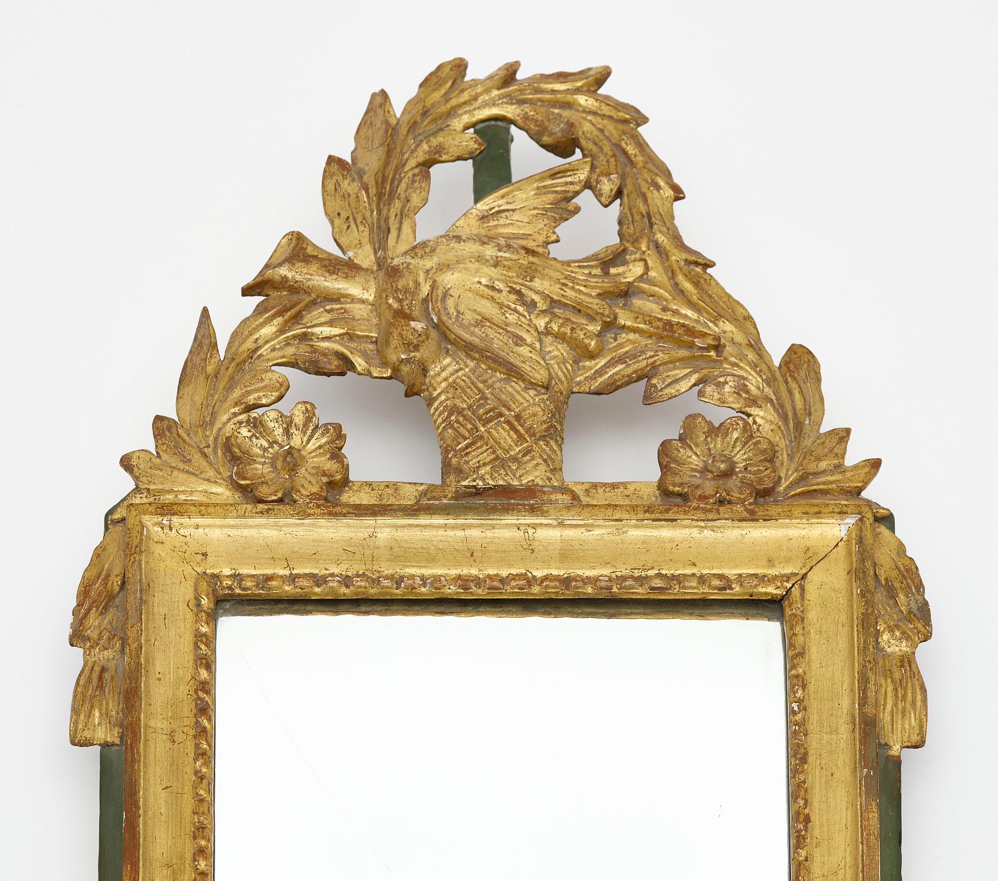 Miroir de France de la période Louis XVI. Cette pièce est faite de bois stuqué sculpté à la main avec un fronton qui présente un oiseau, des motifs floraux et une couronne de laurier. La feuille d'or 24 carats est d'origine, tout comme le miroir au