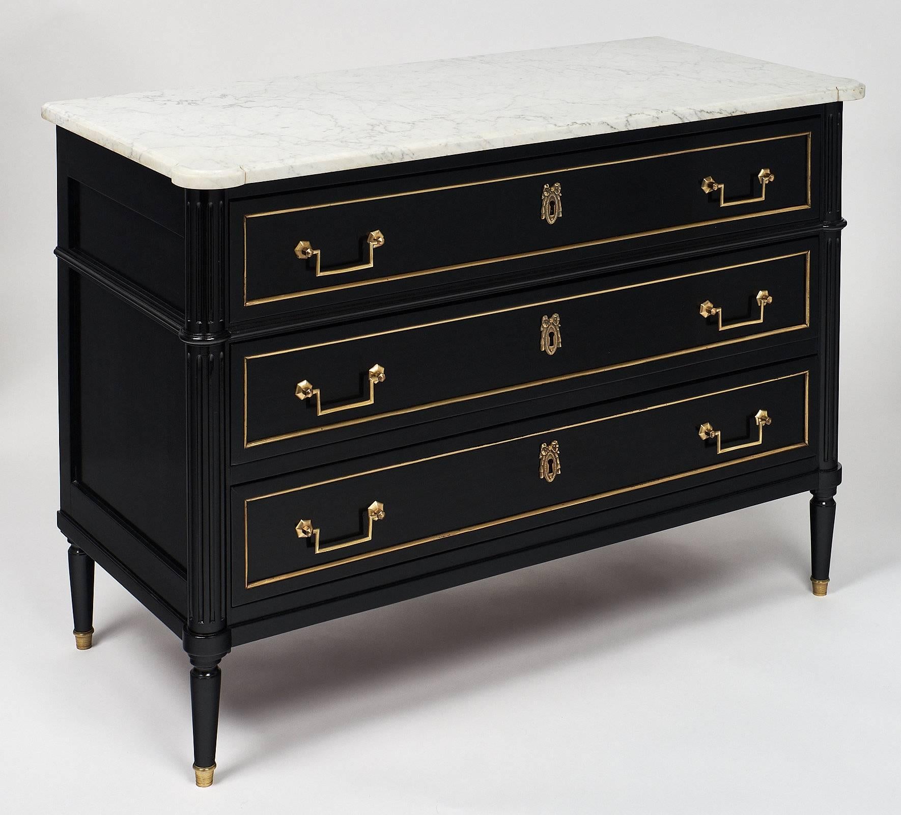 Louis XVI style French antique chest of drawers or “commode”. It features an intact Carrara marble top and three dovetailed drawers with gilt brass handles and hardware. We love the hand-carved fluted details. It is made of mahogany with oak as a