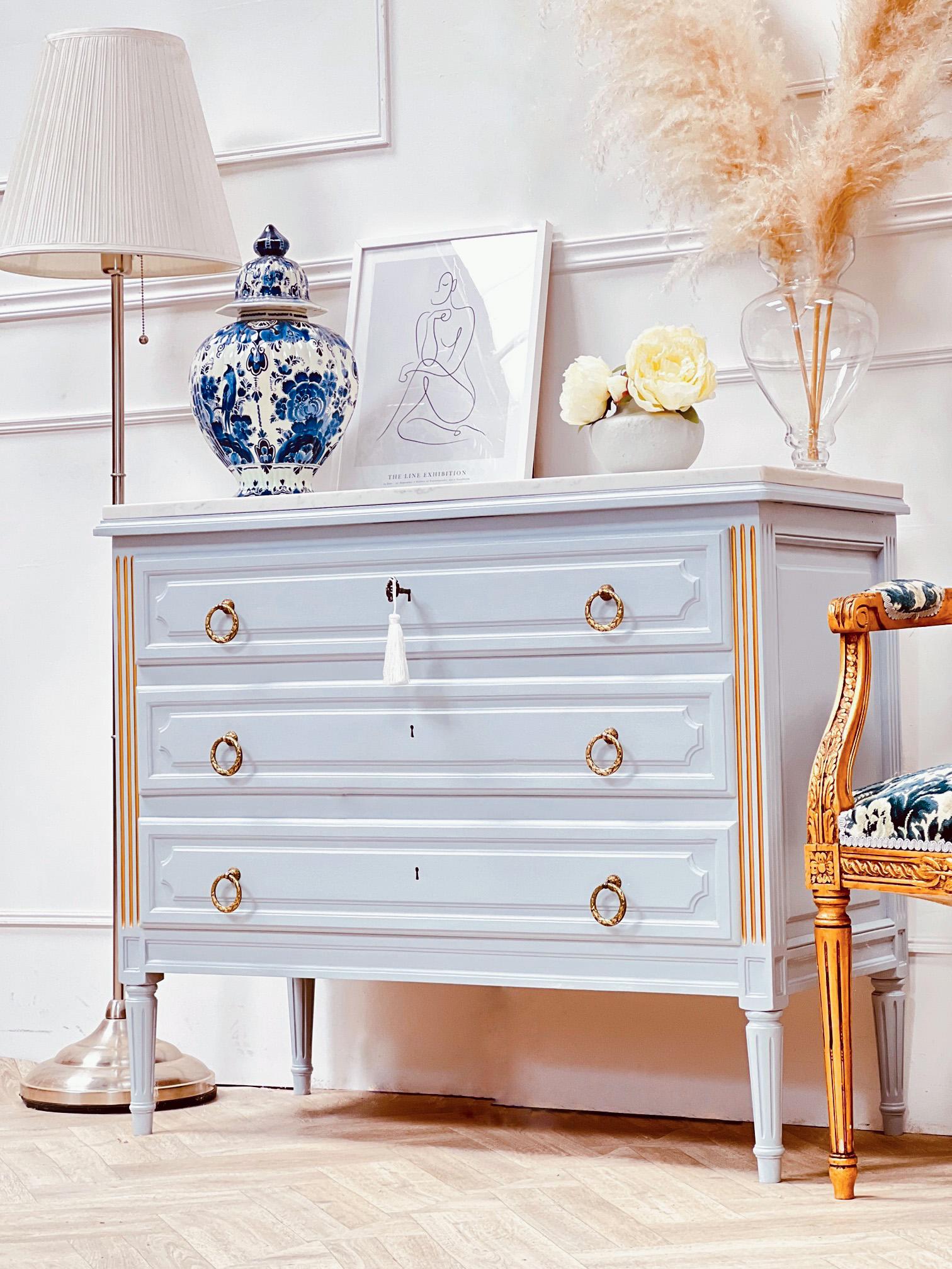 The Piece: 

A beautiful grey blue Louis XVI style chest. Stood on tall fluted legs this medium sized chest has been refinished in a calming blue grey. He cool finish contrasts against her gold original hardware and hand painted details.
Her