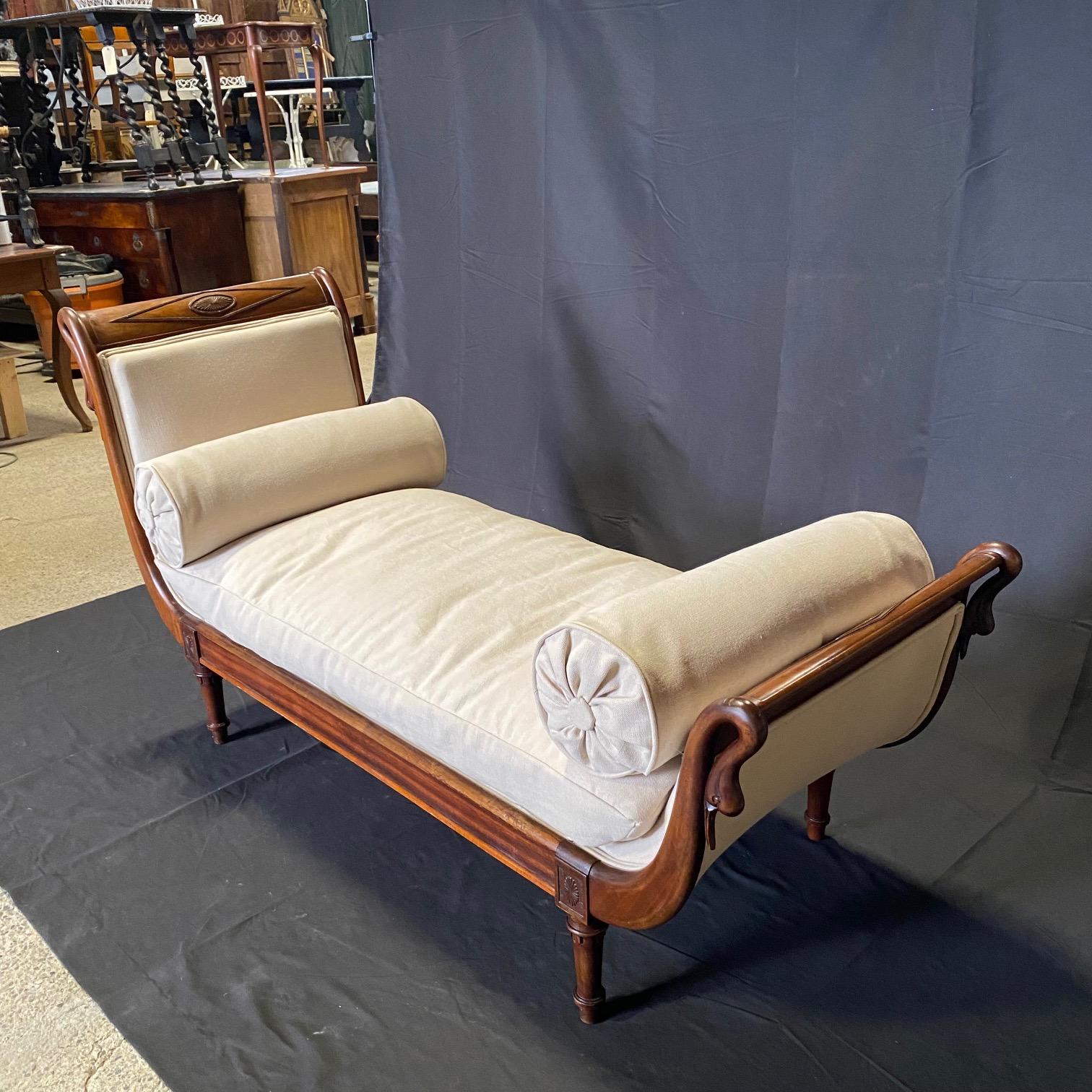 Elegant 19th century French Empire walnut daybed or chaise lounge featuring carved swan neck ends. The cushioned seat is within padded ends of unequal height with gilded swan necked facing boards having diamond crests on each end over a paneled