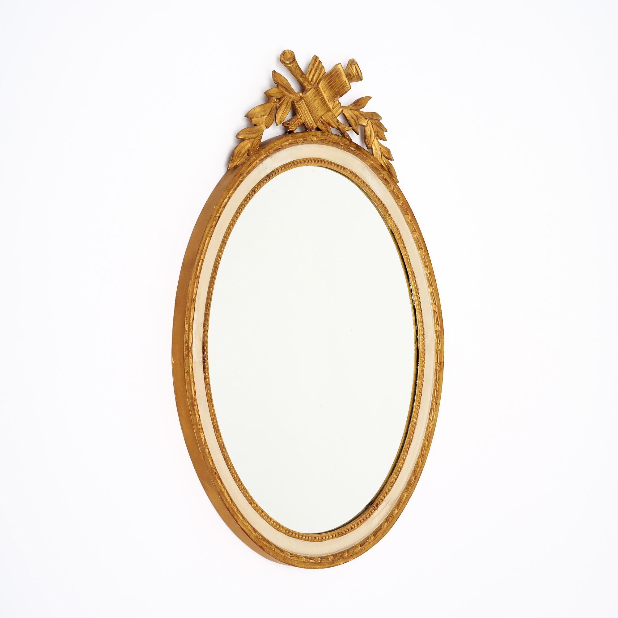 Oval mirror from France featuring a hand-carved frame. The frame, made of wood, supports a central oval mirror original to the piece. The frame itself has a inner cream toned paint, while the trim and hand-carved detail is all finished with a 23