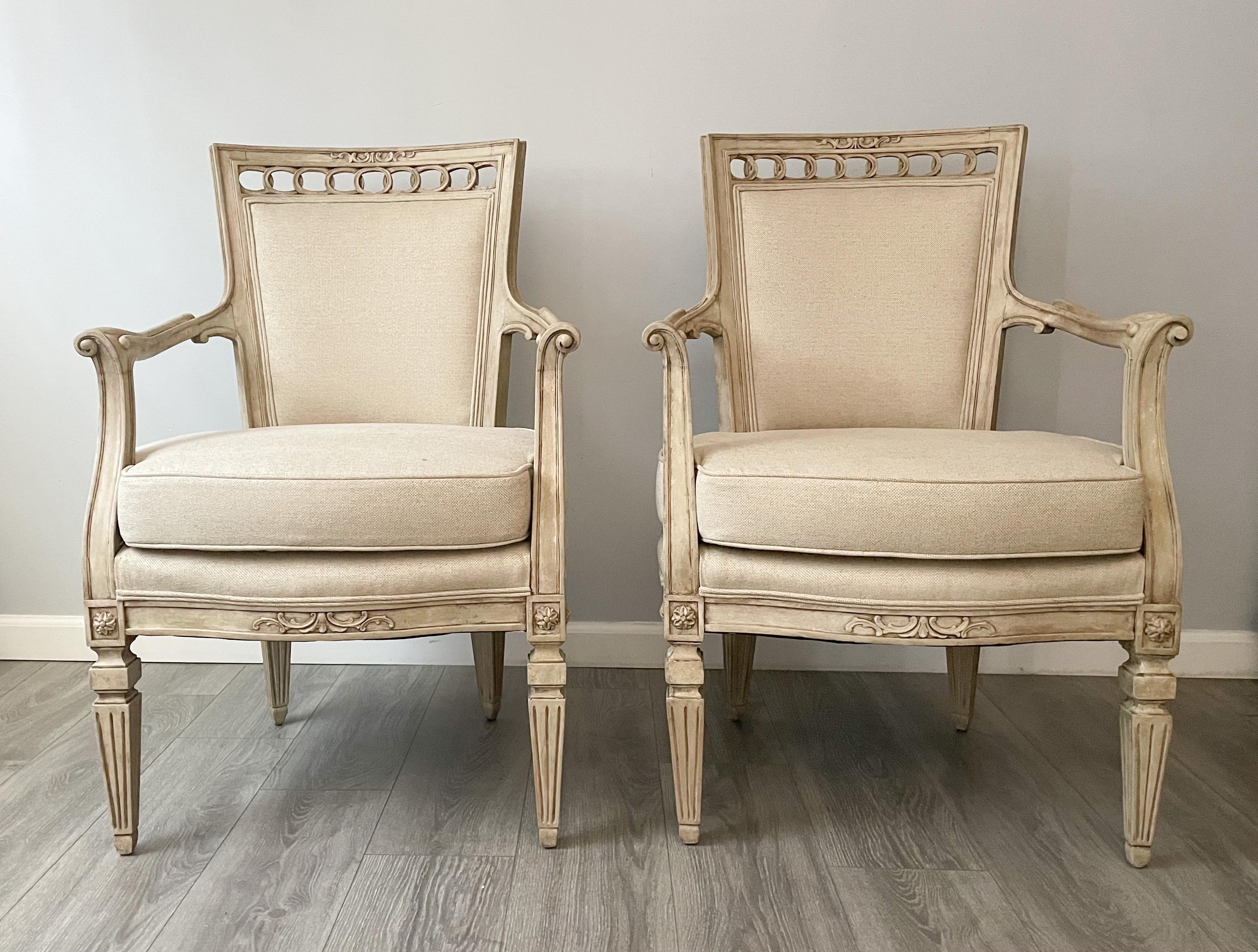 Gorgeous, antique pair of French arm chairs in the neoclassical style.

Each chair consists of an elegantly carved wood frame with a distressed paint finish and new linen upholstery. Loose seat cushions and self-welt details. 

The chairs are
