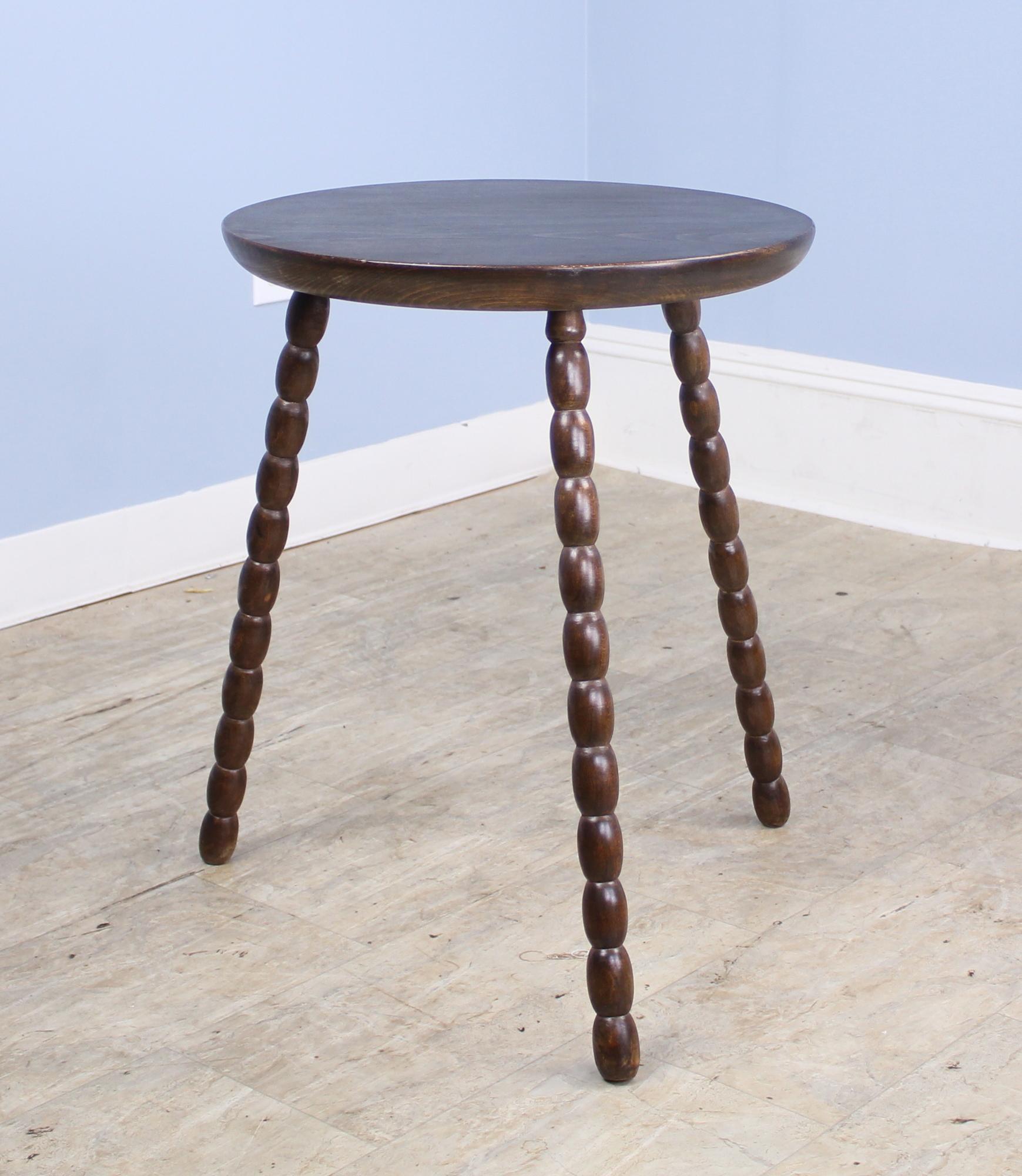 A sleek cricket, lamp, or side table with whimsical bobbin legs. Top has been refinished. Diameter measurement is for the tabletop; there are 22 inches between each leg at the bottom.