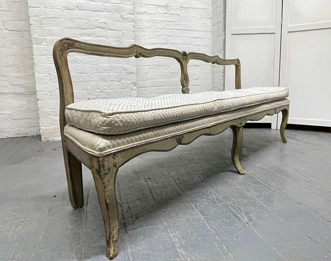 French antique painted bench. The bench has a tufted seat and hand-painted floral designs to the wood frame. This petite bench has a low seat height.