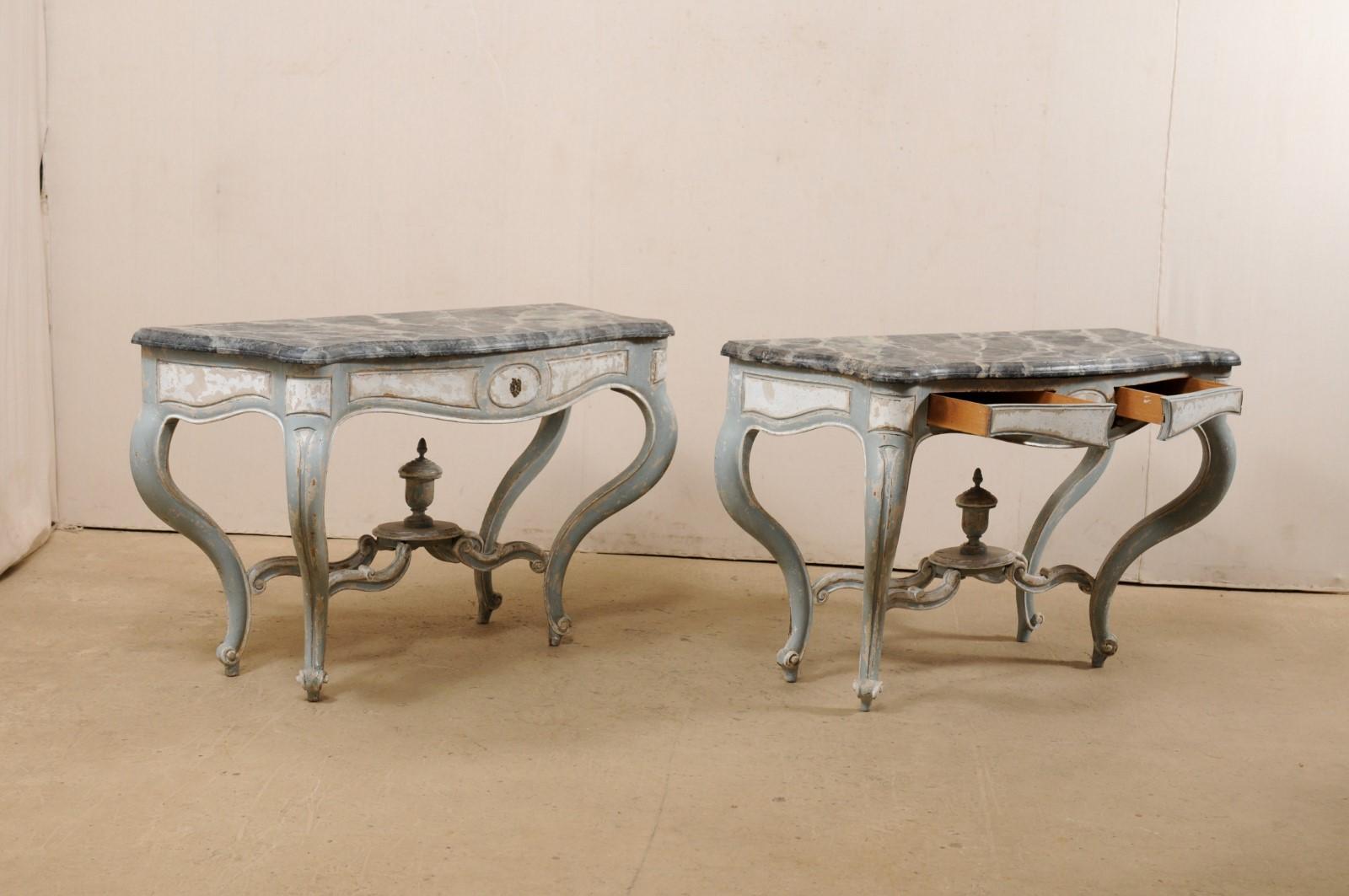 A French pair of carved and painted wood console tables, with faux-marble tops, from early 20th century. This antique pair of tables from France feature an oblong shaped top with flattened backside, curved sides and serpentine shaped front. The