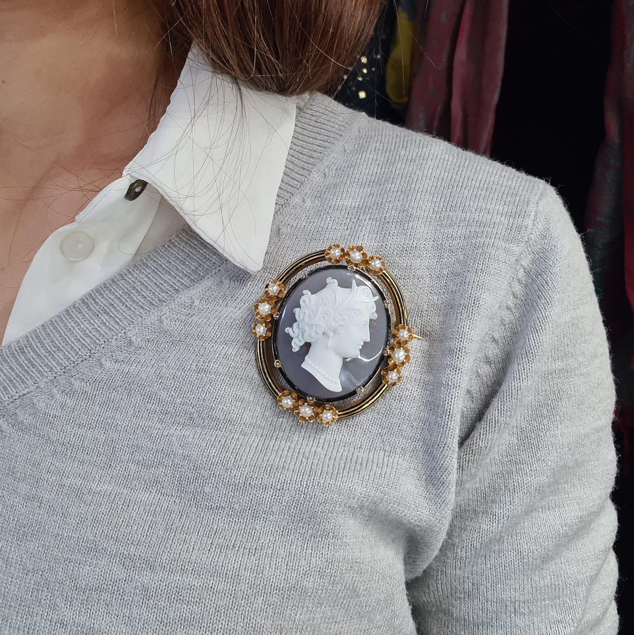A hard stone cameo brooch, set with a cameo of a Roman woman's head, carved in high relief, onto a grey background, in a gold frame with a black enamelled surround, set with natural half pearls and rose-cut diamonds. With a French eagle marks for