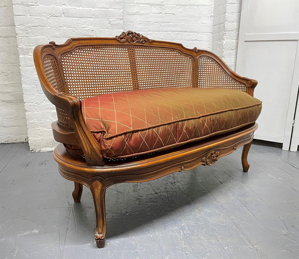 French antique style cane loveseat. The loveseat has a loose cushioned and a cane seat and back. Nice carvings to the top back.