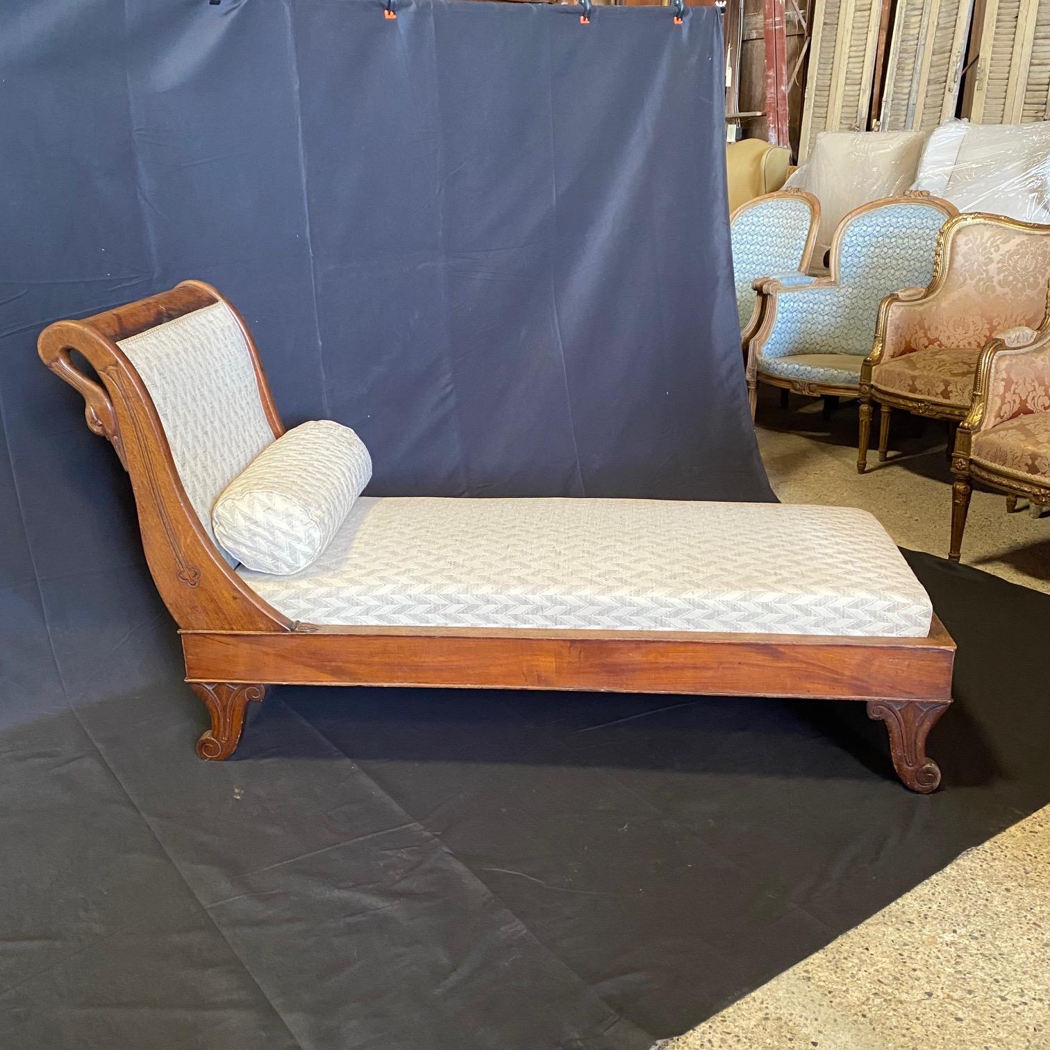 A fine antique French walnut recamier or chaise lounge  with carved swan heads at posts, lovely neutral vintage upholstery and bolster pillow, circa 1930. The chaise rests on four carved tapered escargot feet. Upholstery in good used condition (see