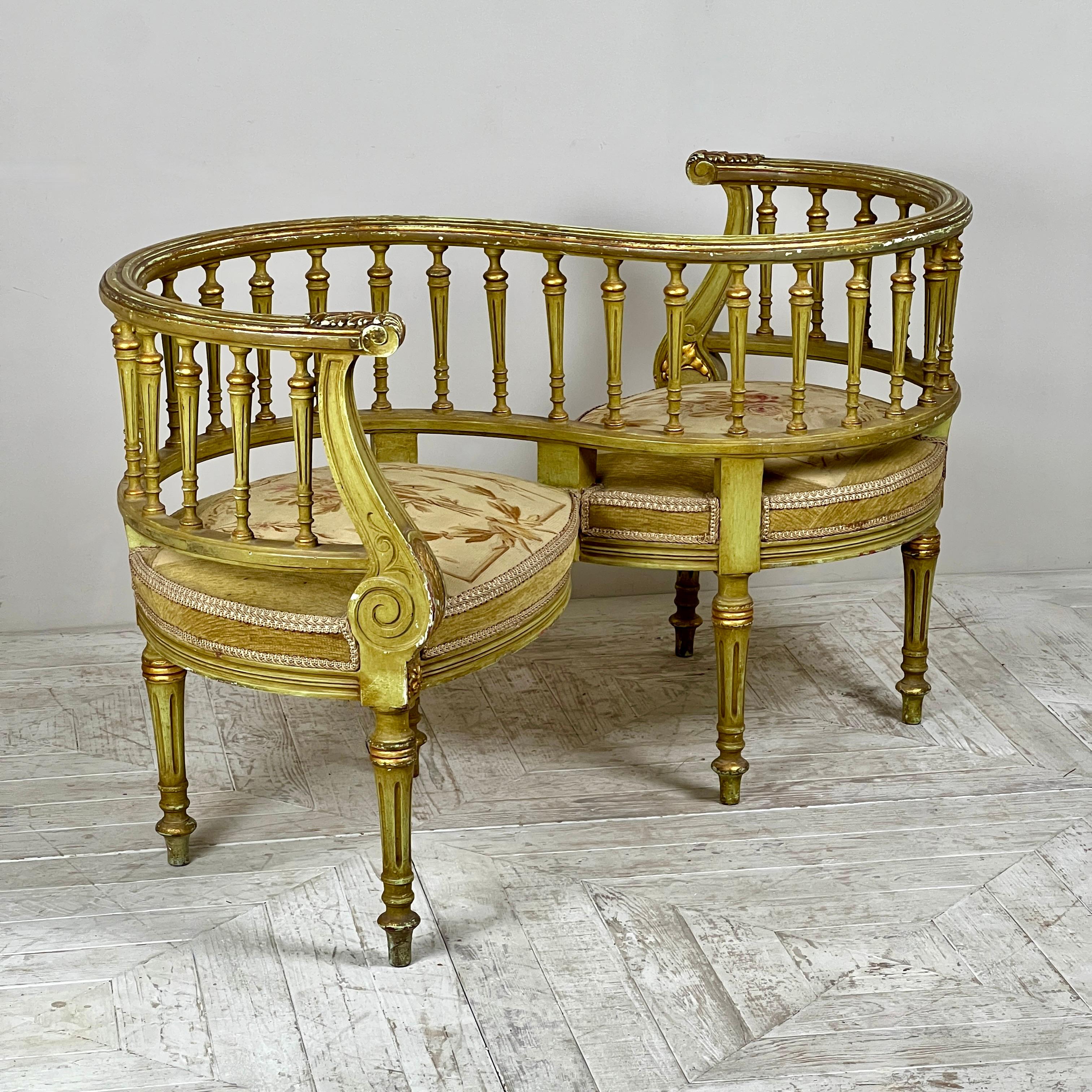 A charming French Antique Painted Tapestry Love Seat, also known as a conversation or Tête-à-Tête seat. The beautifully carved serpentine crest rail, terminating in gilded acanthus leaves, is complemented by elegant sabre-shaped supports. The