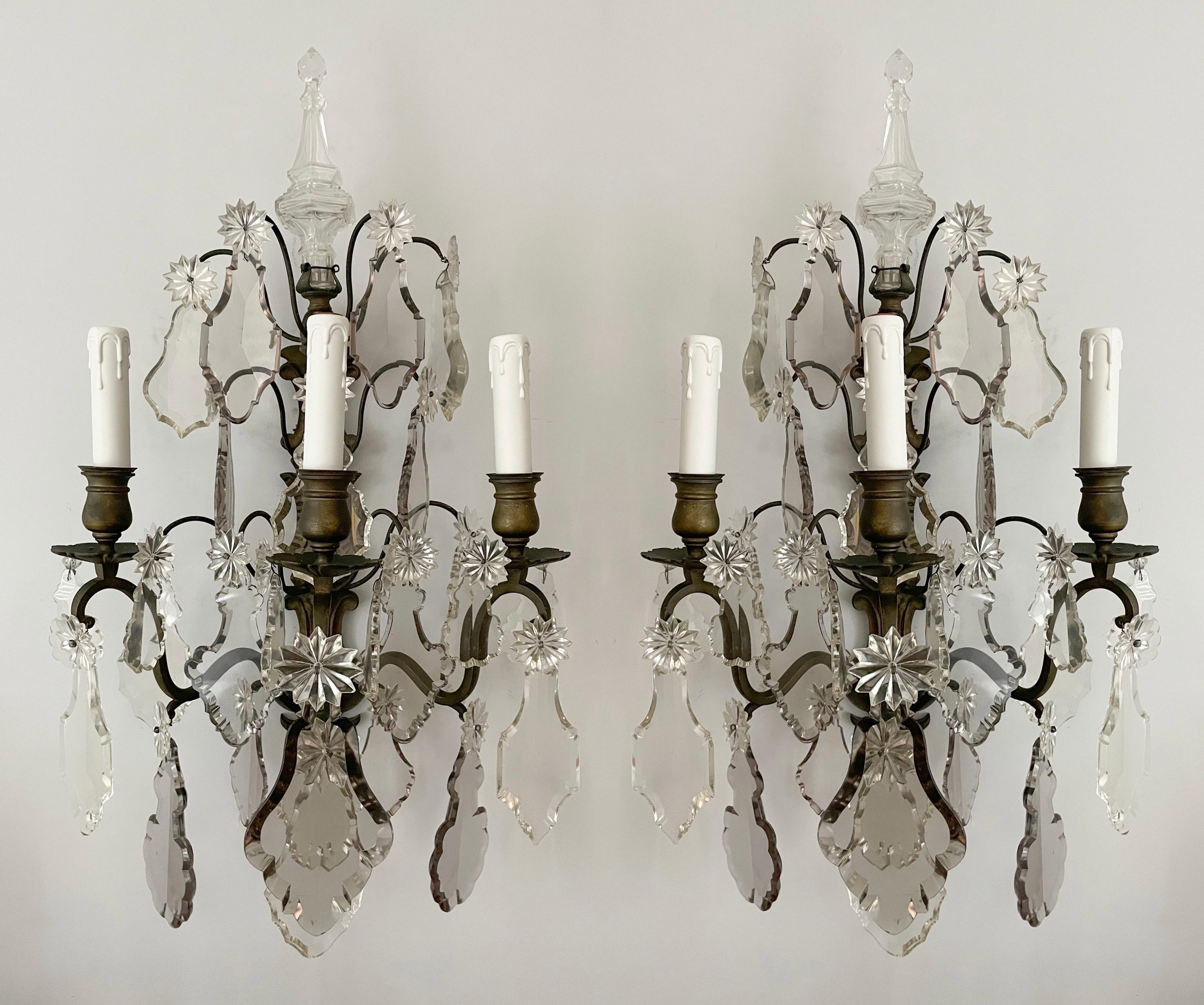 Exceptional, French 1920s crystal and bronze sconces in the Louis XVI style. 

The sconces feature bronze frames adorned with a fine assortment of French crystal pedagogues in clear and smoke hues. Each sconce is crowned with an impressive hollow