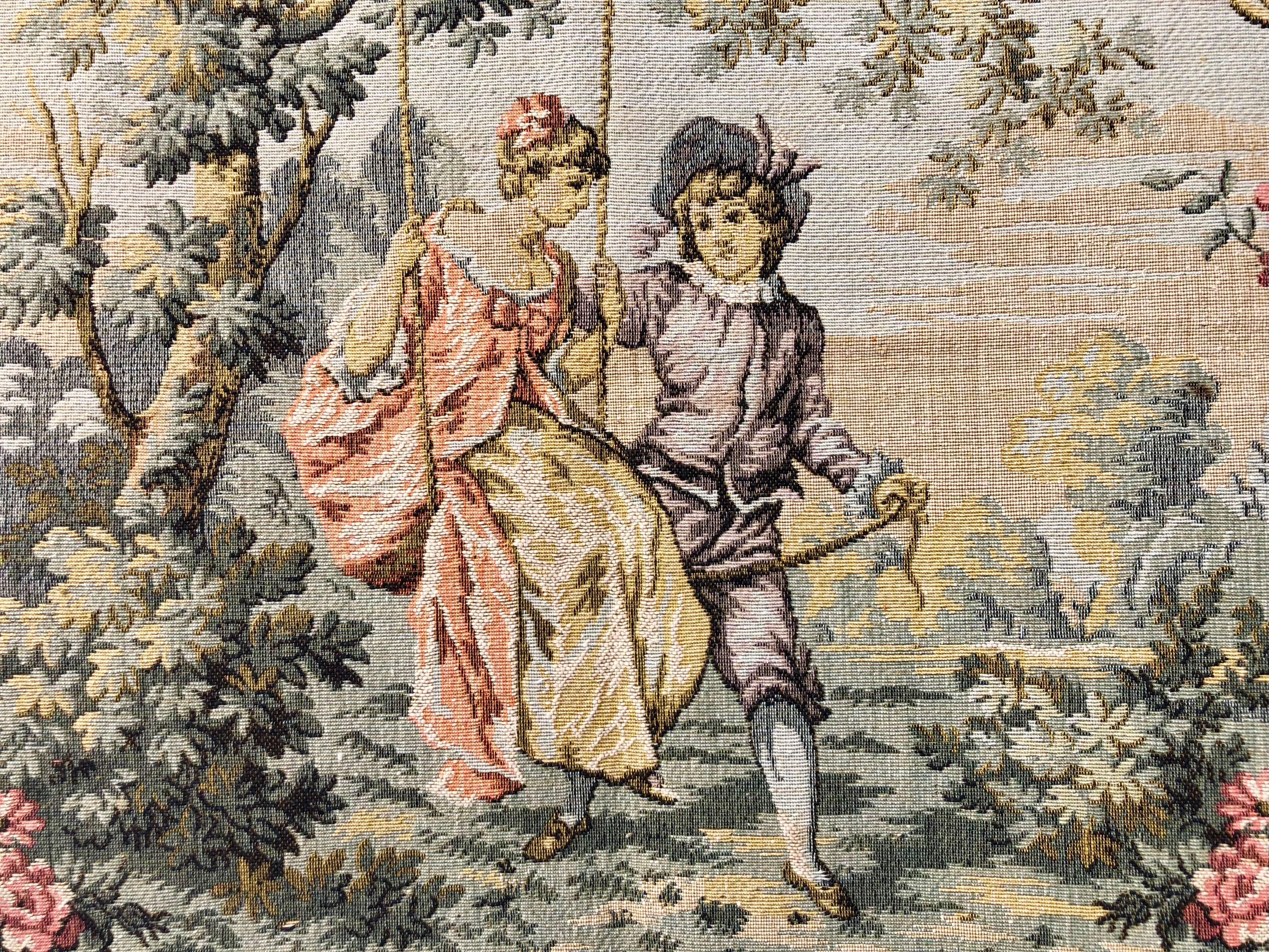 A lovely machine woven jacquard tapestry with multiple colors depicting a pastoral scene of a girl on a swing with her beau. The background color is a pretty green and the scene is surrounded by a woven scroll work design in gold and tan tones. The