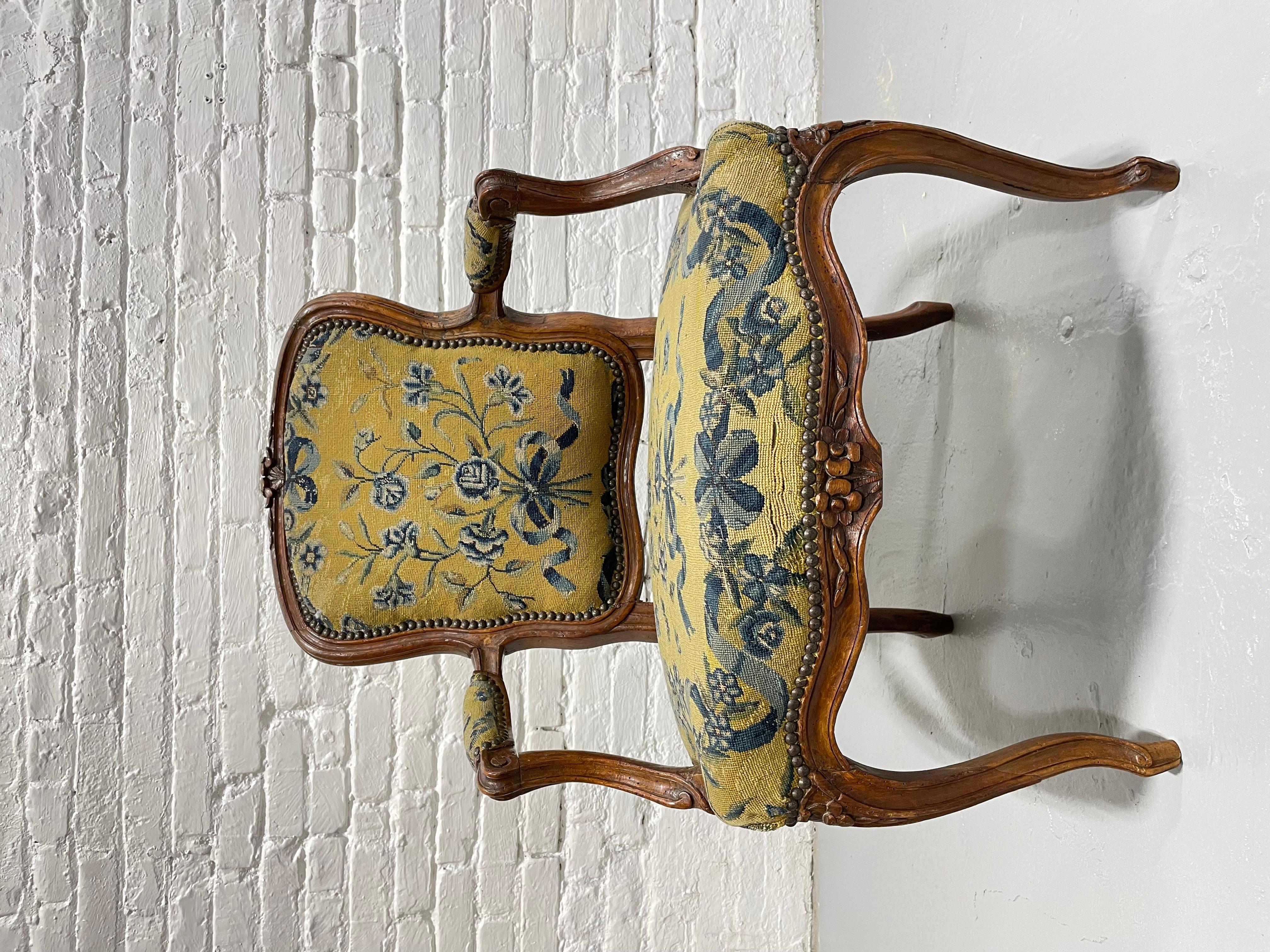 French Antique Walnut Louis XV Walnut Armchair featuring deep hand carved elegant flower and foliage designs. Made in France circa mid-1700’s. The upholstery is a lovely tapestry of yellow with blue floral patterned design. Nice antique condition