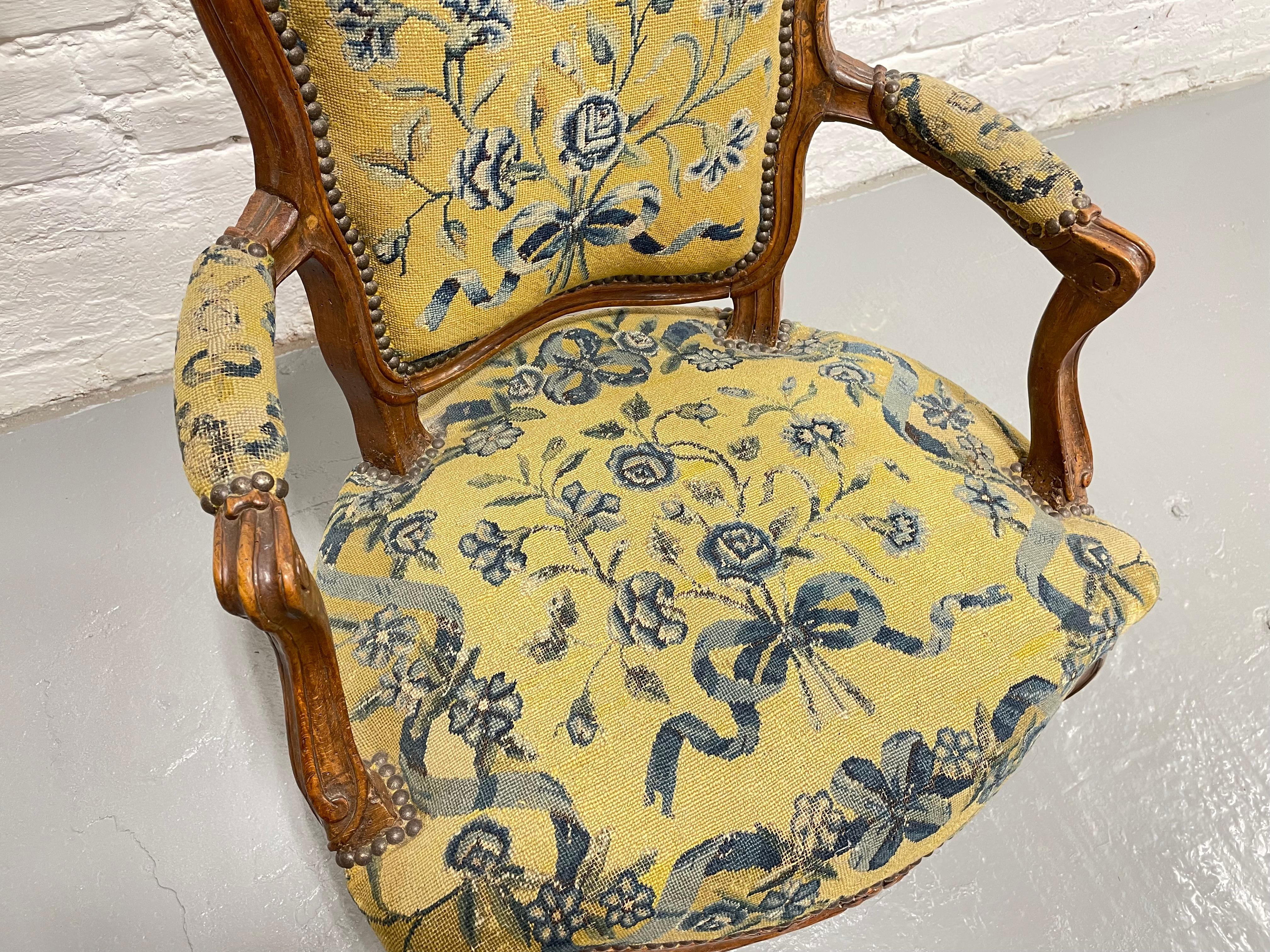 Fauteuil Louis XV en noyer ancien, profondément sculpté à la main d'élégants motifs de fleurs et de feuillages. Fabriqué en France vers le milieu des années 1700. La tapisserie est une belle tapisserie jaune à motifs floraux bleus. Belle condition