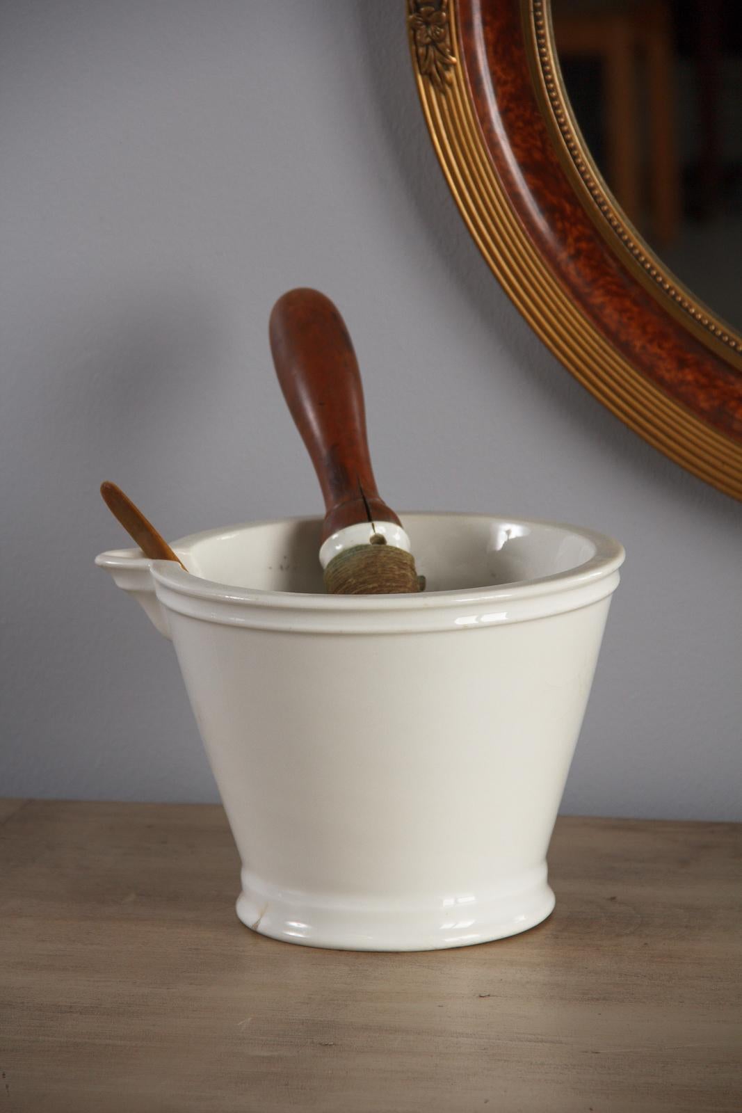 A large, glazed ceramic pharmacist's mortar and pestle for apothecary use, circa late 1800s. White ceramic form with a flared top and tapered base, molding at the foot and at the rim. The pour spot is angled and level with the rim. Smoothly glazed