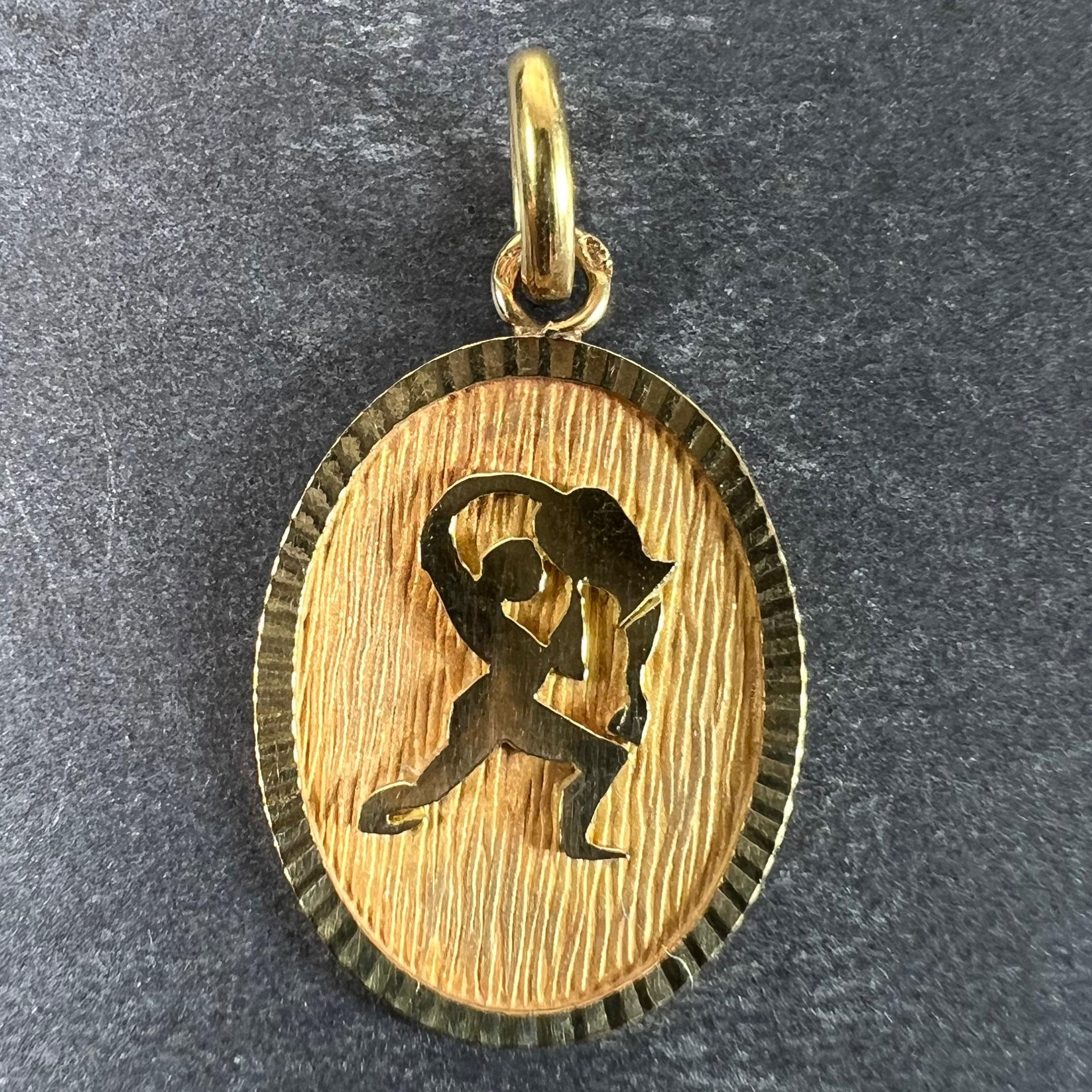 Pendentif à breloques français en or jaune 18 carats (18K) conçu comme une médaille ovale avec un renfoncement mat représentant une personne versant de l'eau d'un vase représentant le signe astrologique du zodiaque du Verseau. Estampillé de la tête