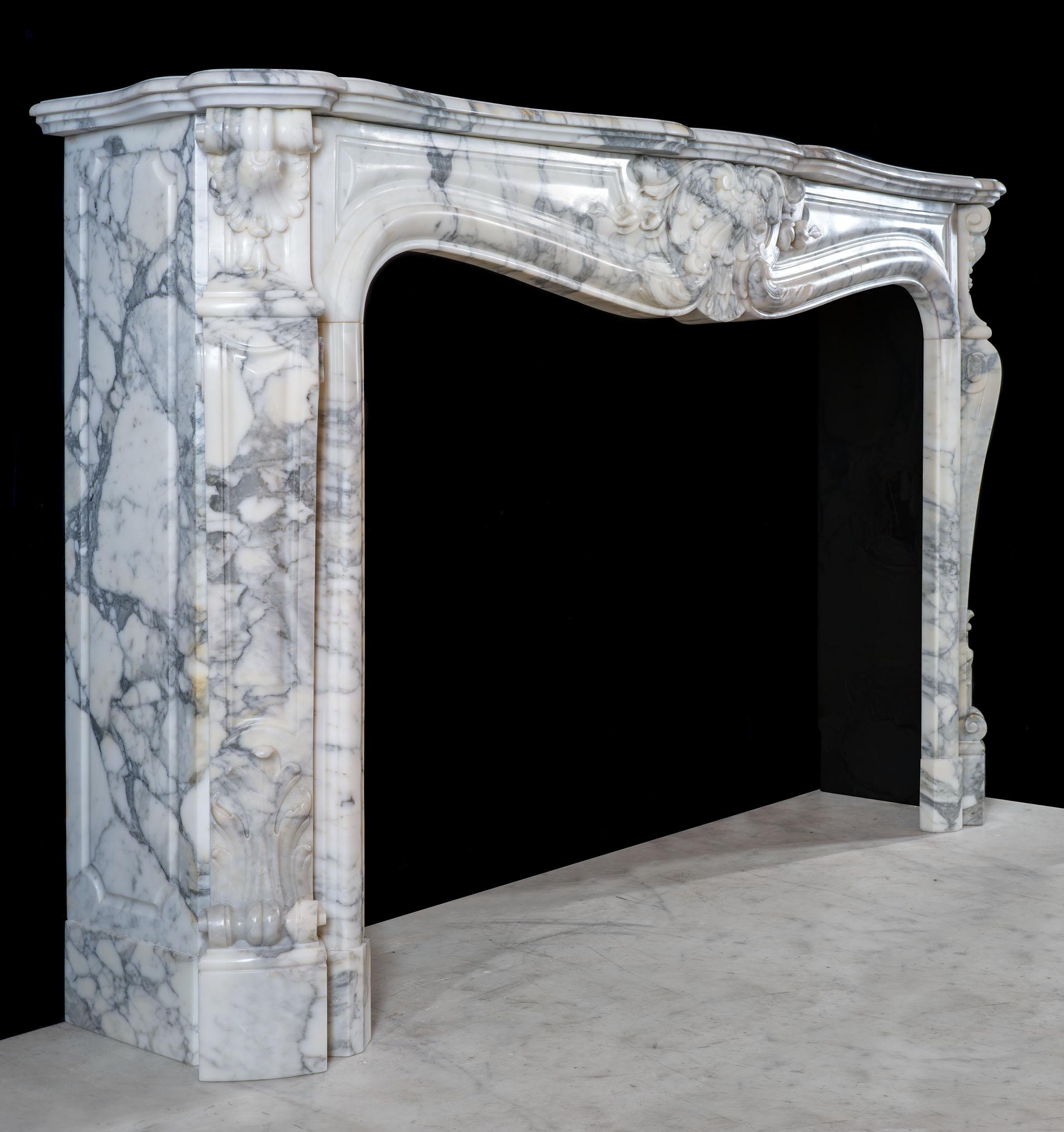 Une belle et grande cheminée rococo française Louis XV en marbre arabescato magnifiquement veiné. La tablette serpentine se trouve au-dessus de la frise lambrissée qui est centrée par un cartouche d'acanthe spectaculaire. Les blocs d'extrémité à