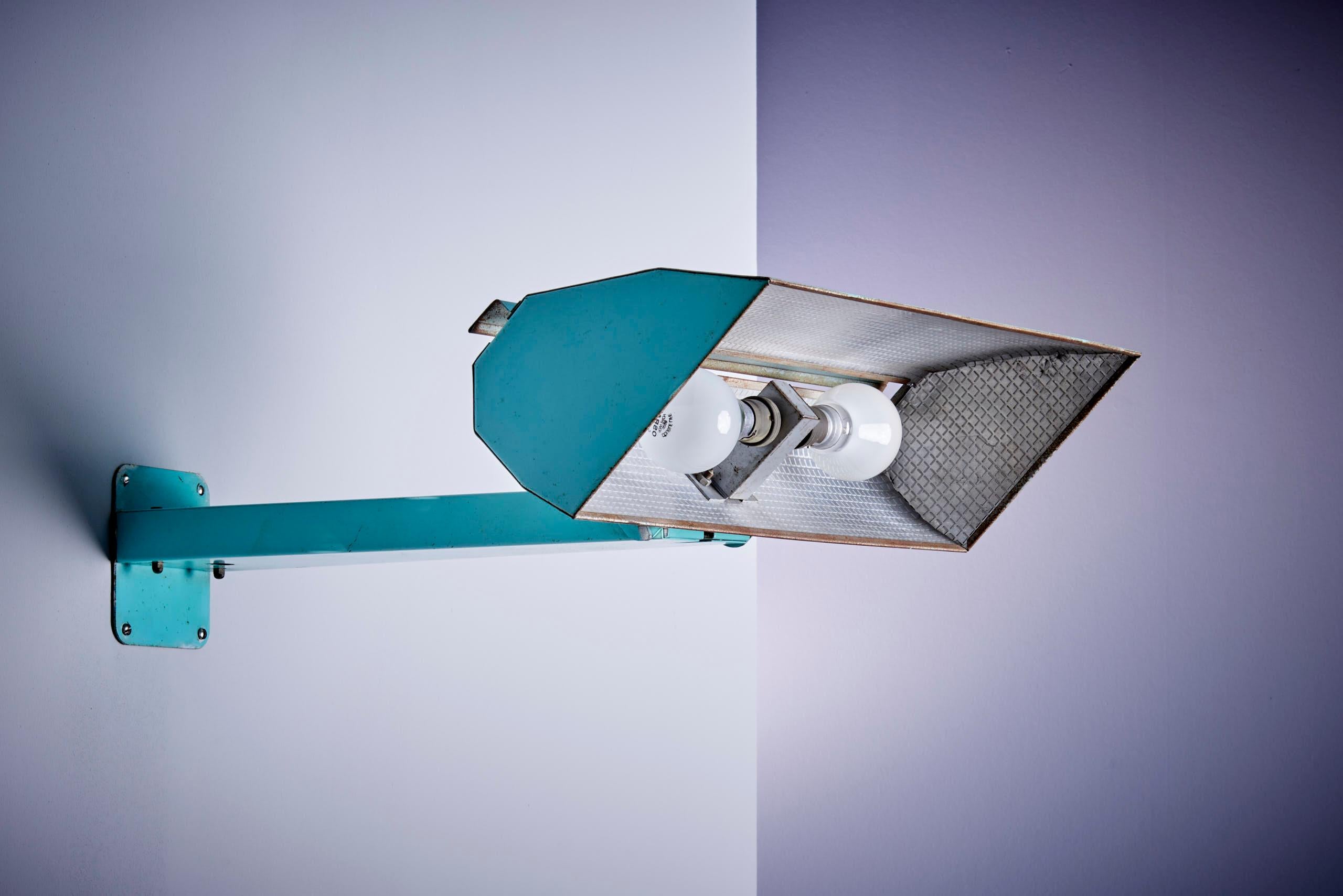 Este aplique francés de mediados de siglo tiene una estructura metálica turquesa y una pantalla geométrica con dos bombillas detrás de un difusor texturizado. Su diseño atrevido e industrial añade un toque retro a cualquier espacio.
