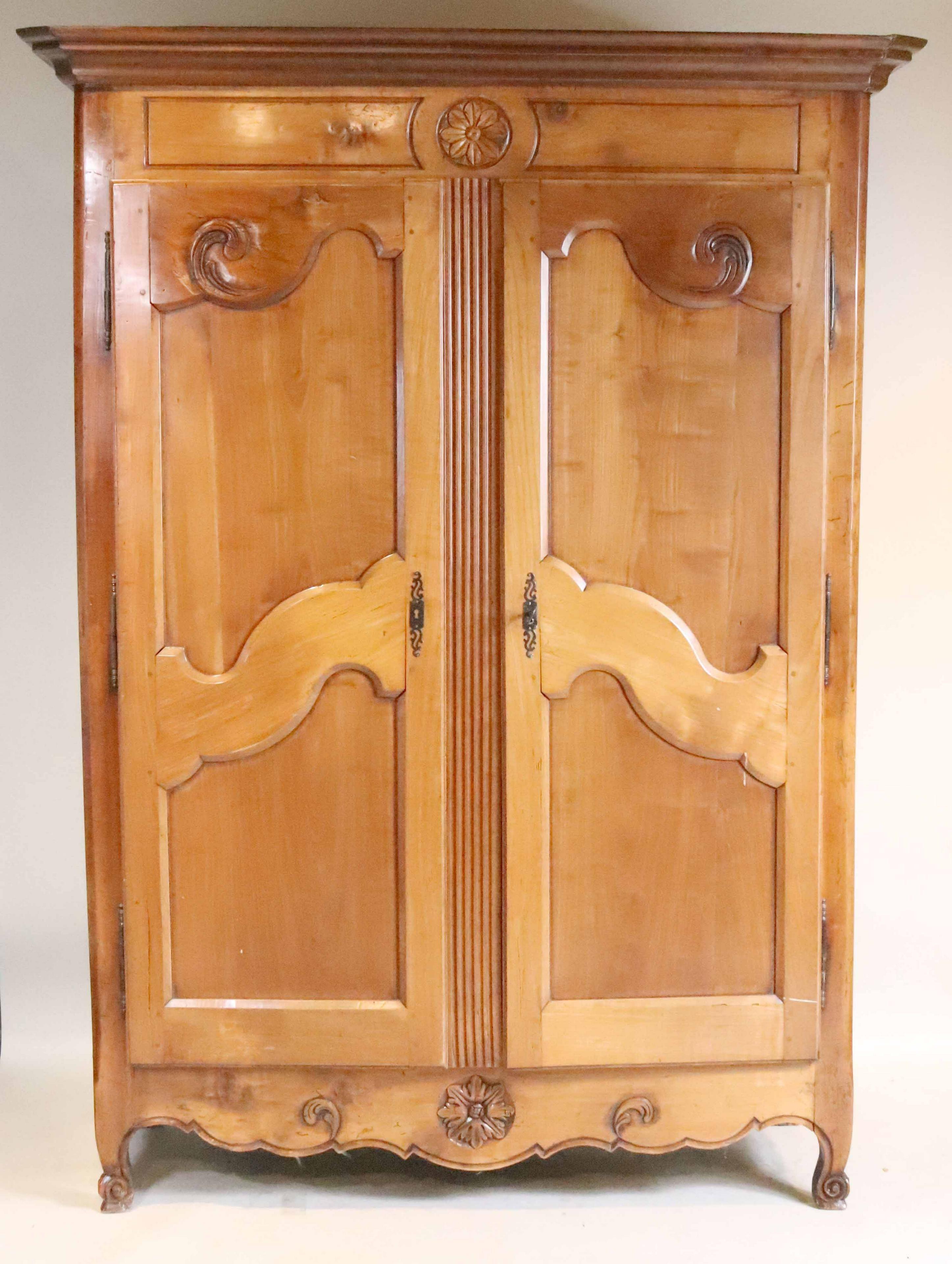 A classic French provincial Louis XV period armoire in fruitwood, circa 1780, with interior removable shelves, beautifully carved and paneled doors with carved flowers above and below on the crest and apron. The feet are carved 