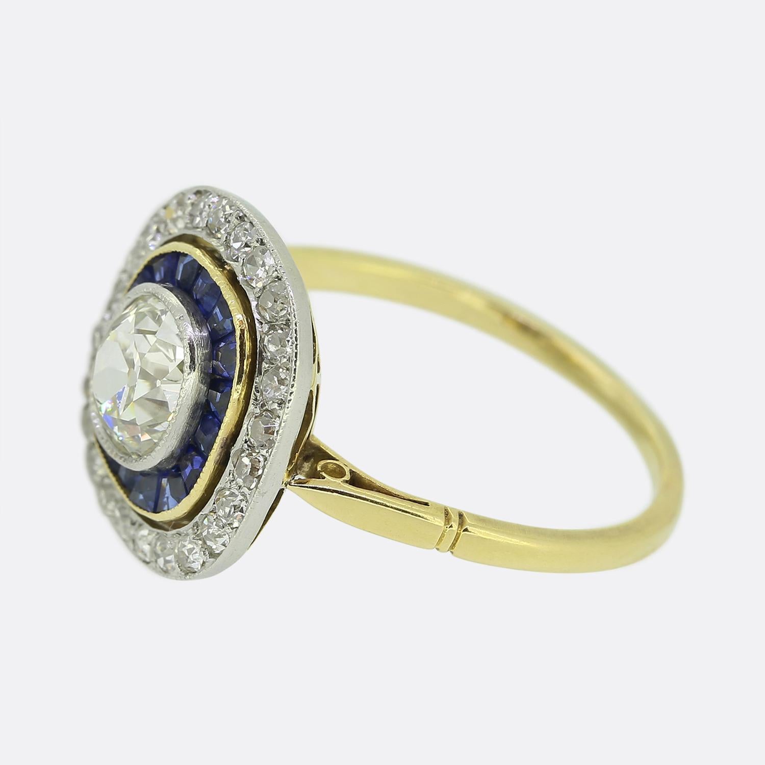 Here we have a stunning cluster ring taken from a time when the Art Deco style was continuing to revolutionise the world of design. A single old cushion cut diamond sits proud at the centre of the face in a fine platinum milgrain setting. This