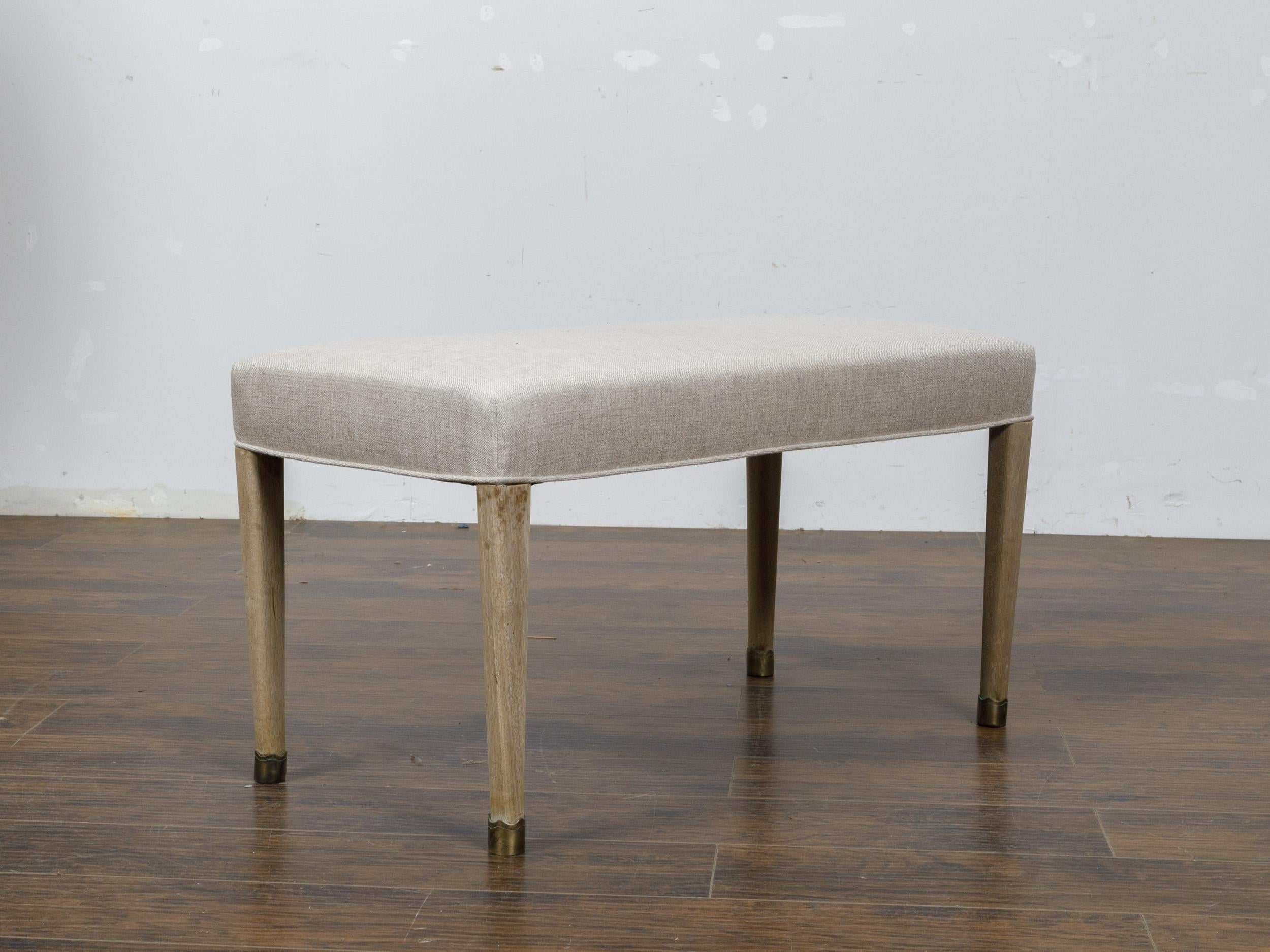 A French Art Deco bleached walnut bench from circa 1930 with brass feet and new custom linen upholstery. This exquisite French Art Deco bench, dating back to circa 1930, elegantly combines the timeless appeal of bleached walnut with contemporary
