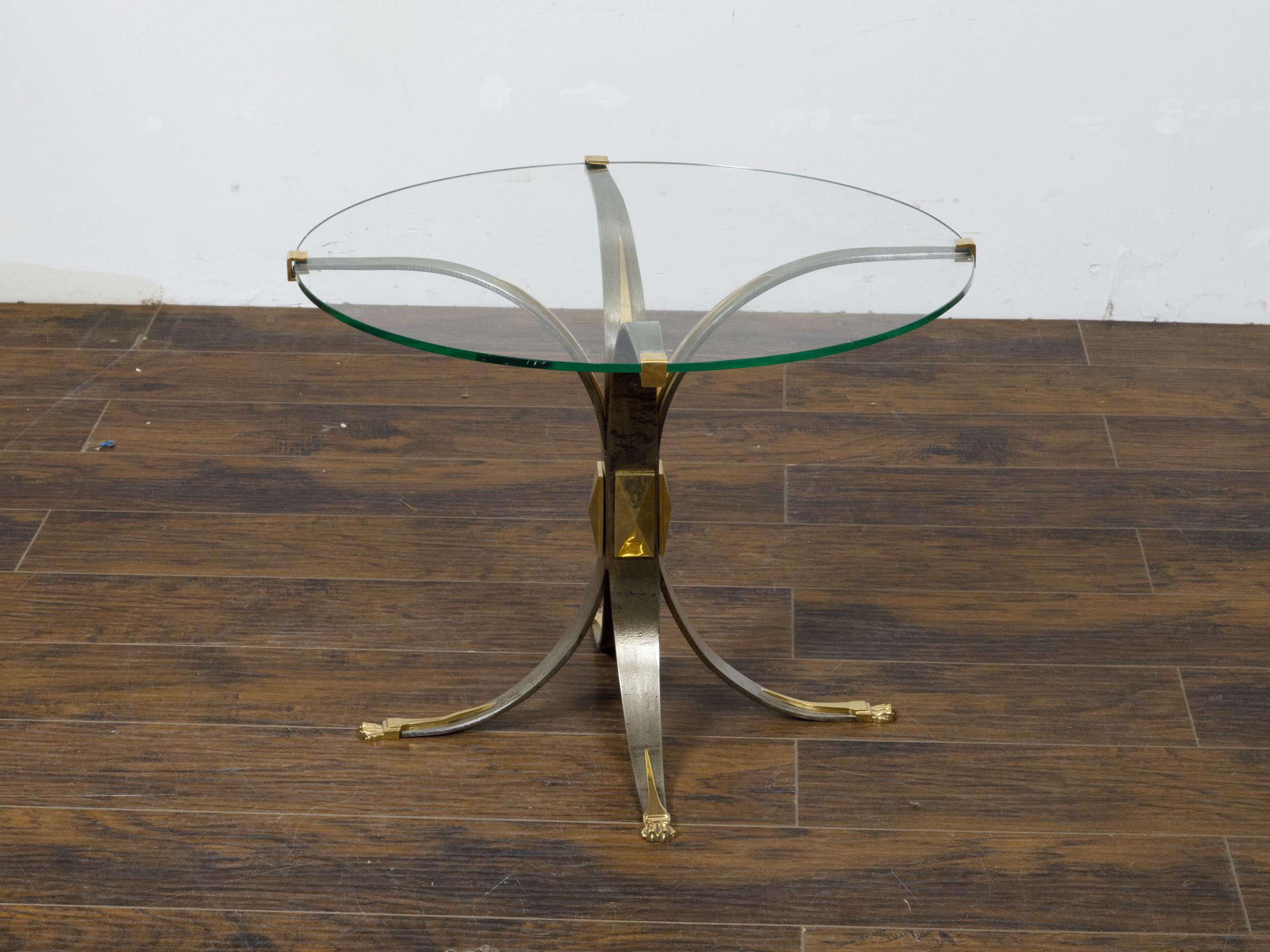 A French Art Deco period steel and brass drinks table from circa 1930, with circular glass top, four splaying legs and lion paw feet. This sophisticated French Art Deco drinks table, dating back to around 1930, is a paragon of the era's penchant for