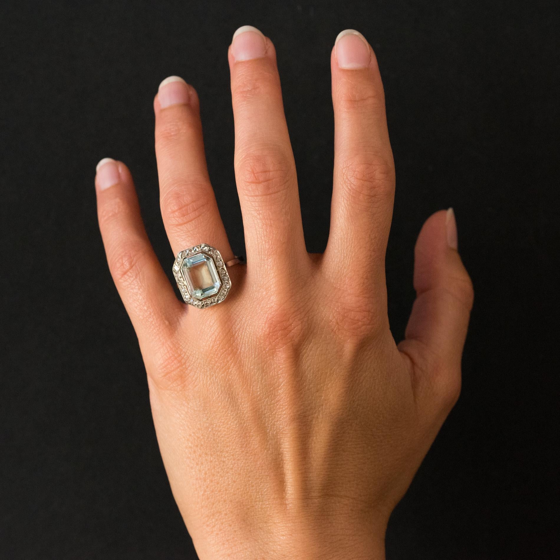 Ring in 18 karats white gold, eagle's head hallmark.
Elegant antique ring, it is set in the center of a degrees-cut aquamarine, set with millegrains. The entourage is composed of 22 rose- cut diamonds. The mounting is pierced and flat on the