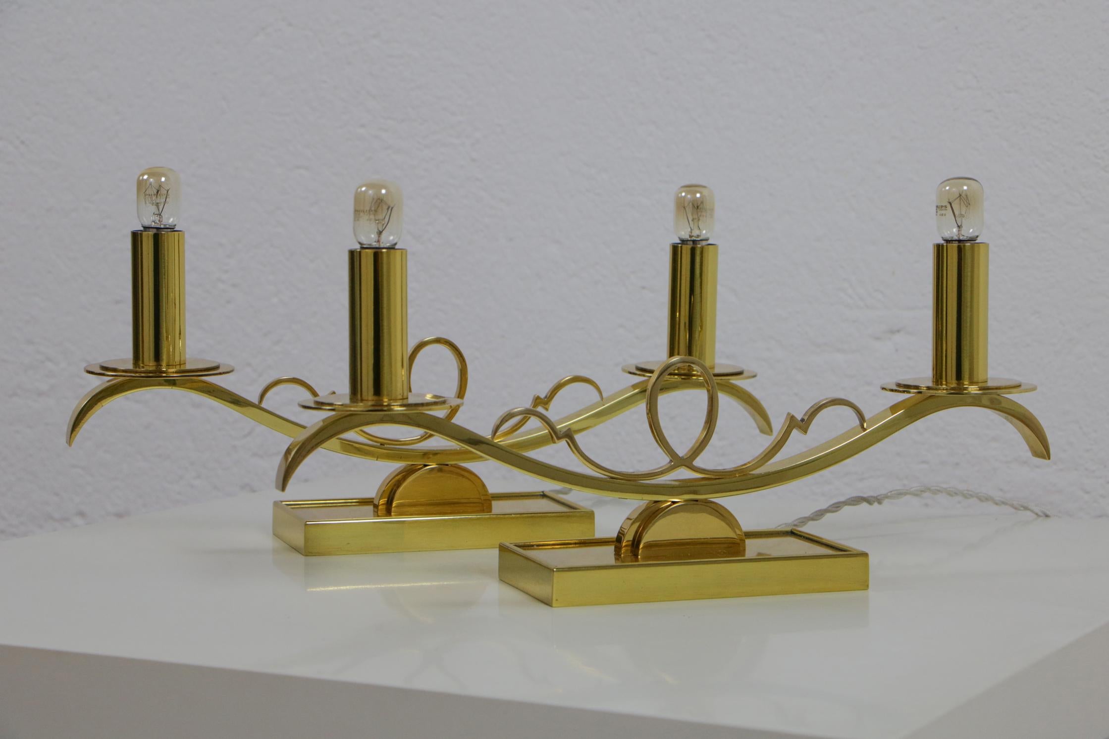 Una splendida coppia di due lampade da tavolo in ottone di ispirazione Art Déco degli anni '30, ciascuna con due prese B15d e finitura lucida. I componenti in ottone sono realizzati con un'attenzione ai dettagli che ricorda quella di un orafo