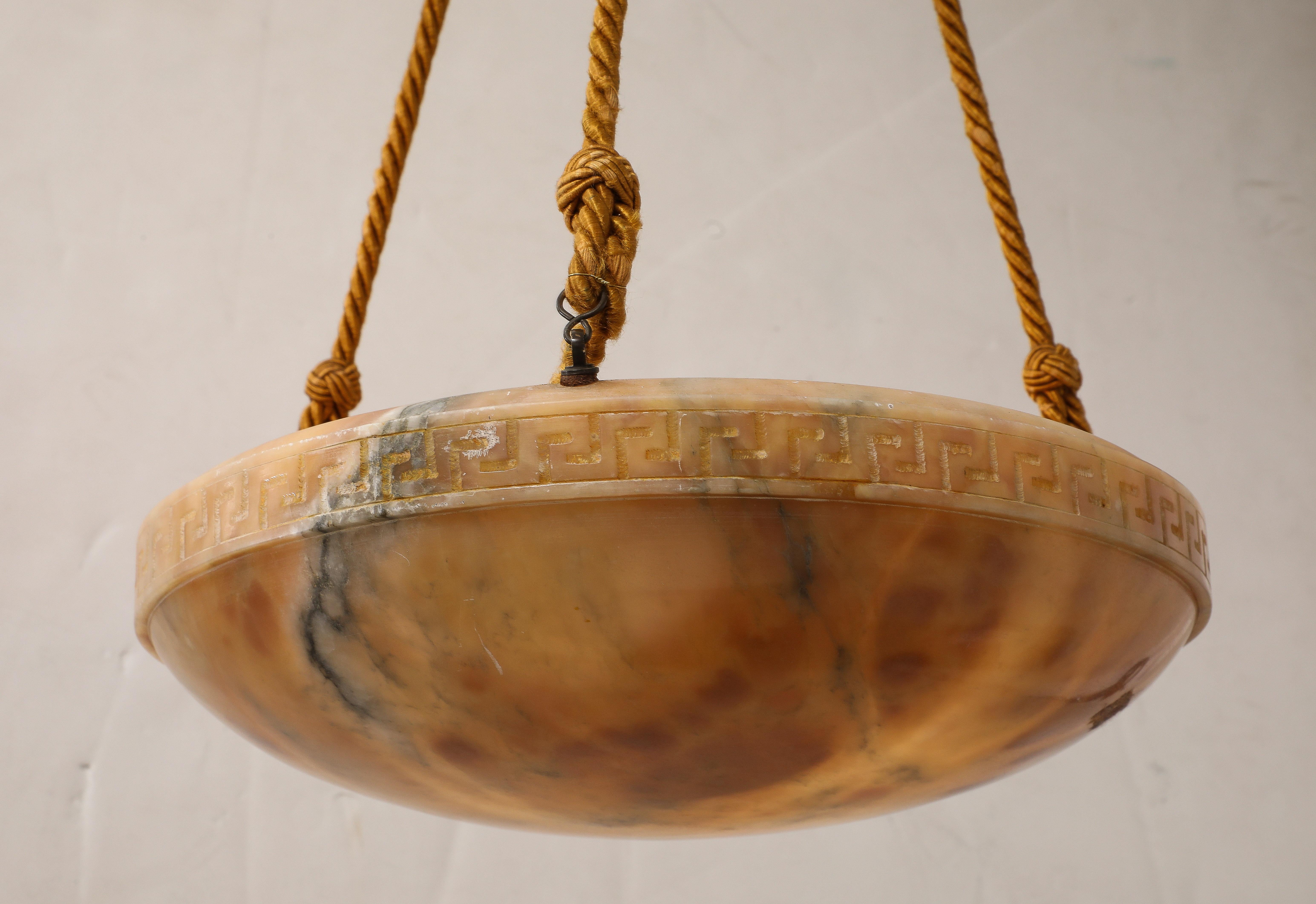 A fine French Art Deco alabaster chandelier with Greek key carved motif, with silk cording and alabaster canopy.  The natural coloration of the stone creates a warm and inviting glow.  Newly rewired for US standards,
France, circa 1940 
Size: 30