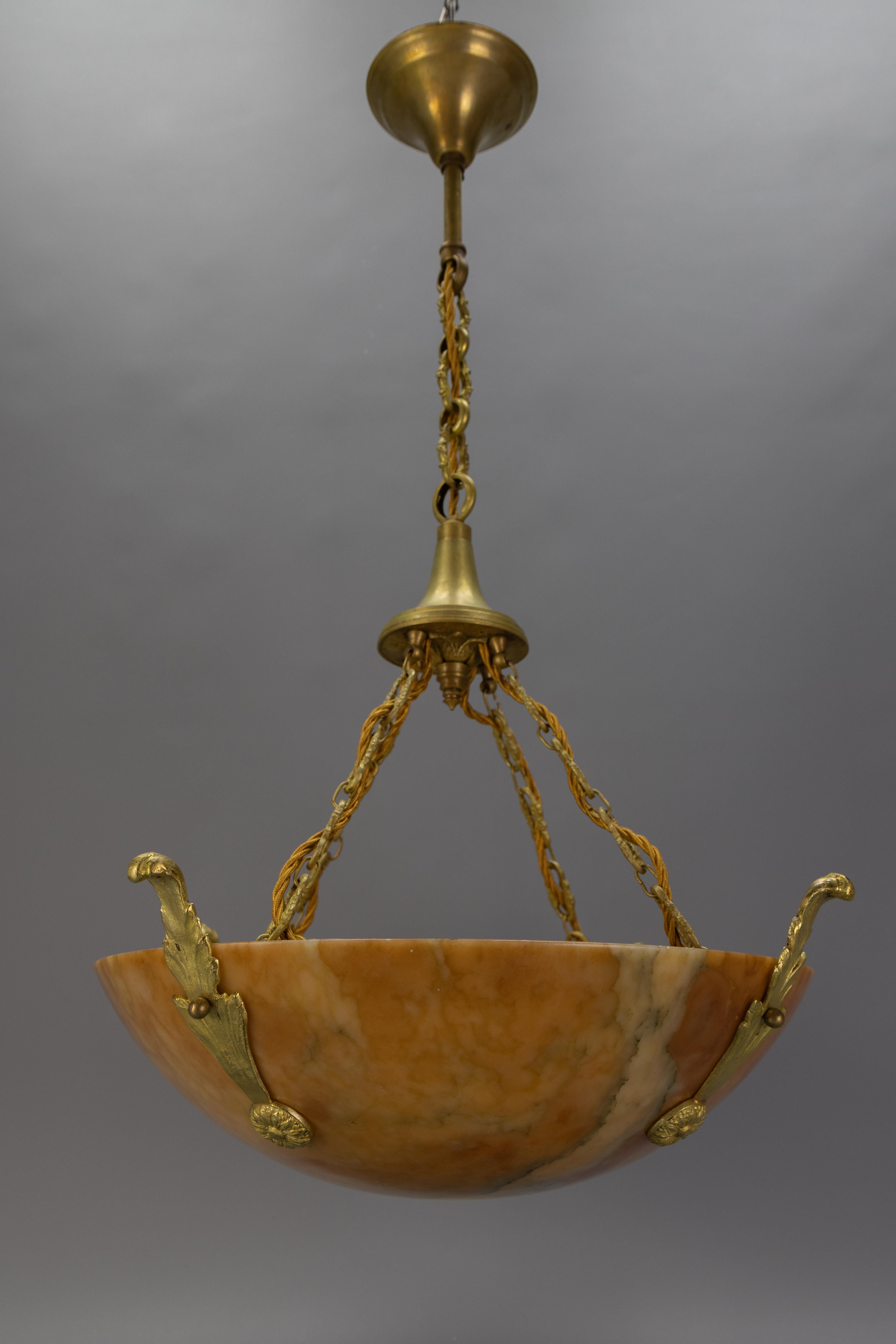 Lampada a sospensione in bronzo e alabastro color ambra dell'Art Déco francese del 1920 circa. 
Questo affascinante lampadario a sospensione a quattro luci presenta un paralume in alabastro con una combinazione di tonalità arancioni e beige più