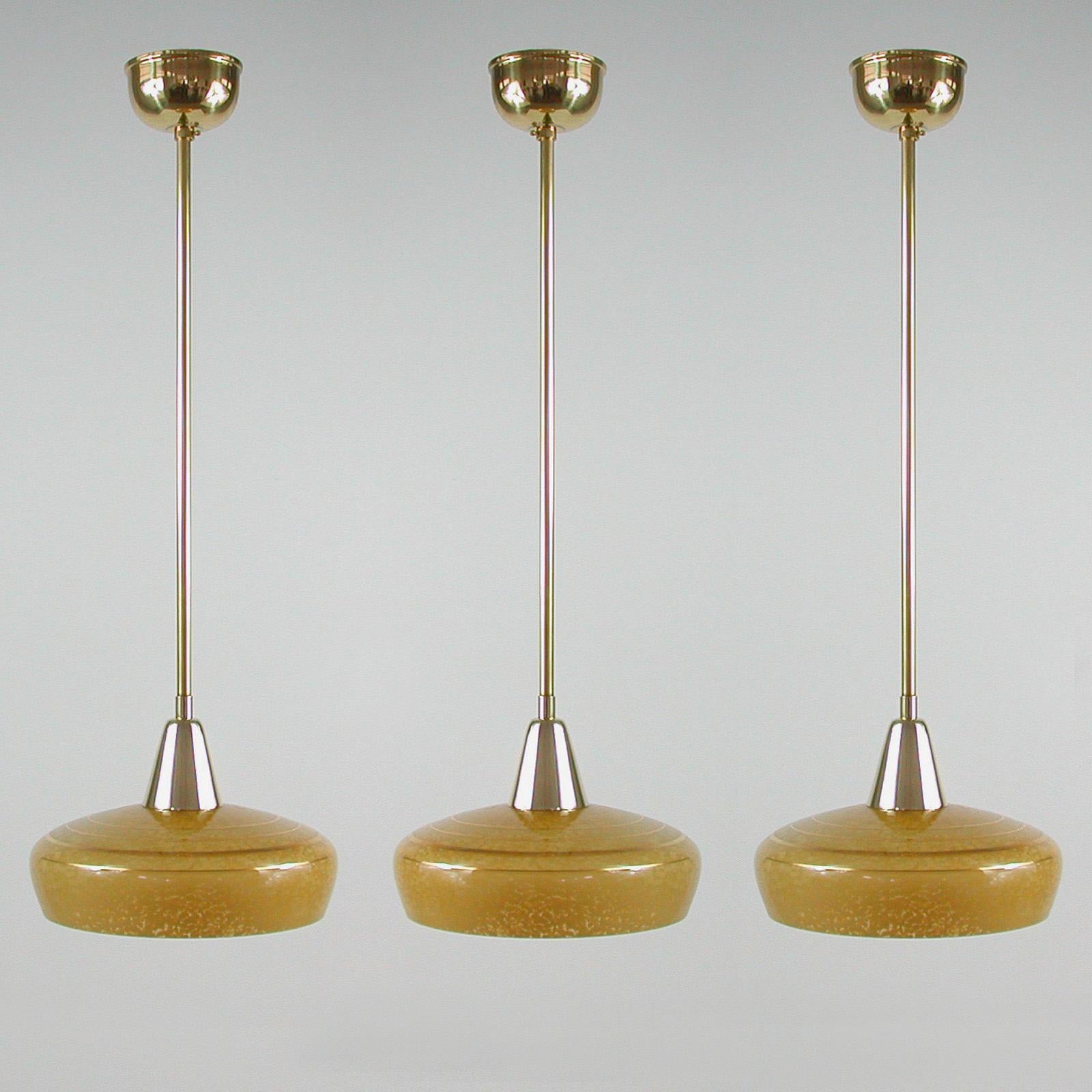 These elegant pendants were designed and made in France in the 1930s-1940s. The lamps are made of brass and have got an amber or honey colored mottled glass shade with golden decor. Good vintage condition with one E27 socket. There is some minor