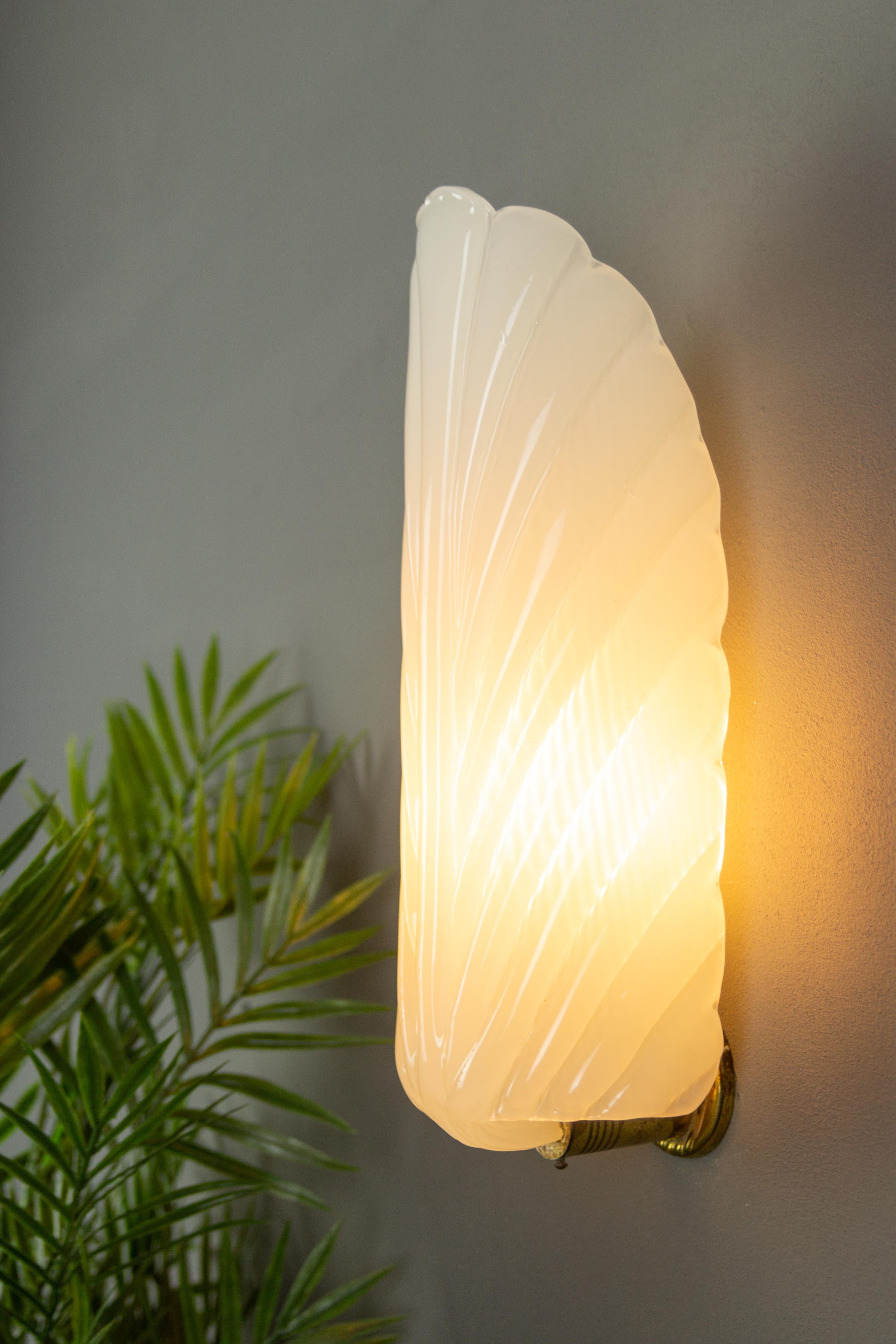 An elegant Art Deco period opaline white glass wall light in the style of André Arbus. The beautiful feather-shaped glass shade is held by a brass wall mount. 
One socket for the E14 size light bulb.
Dimensions: height: 32 cm / 12.6 in; width: 9