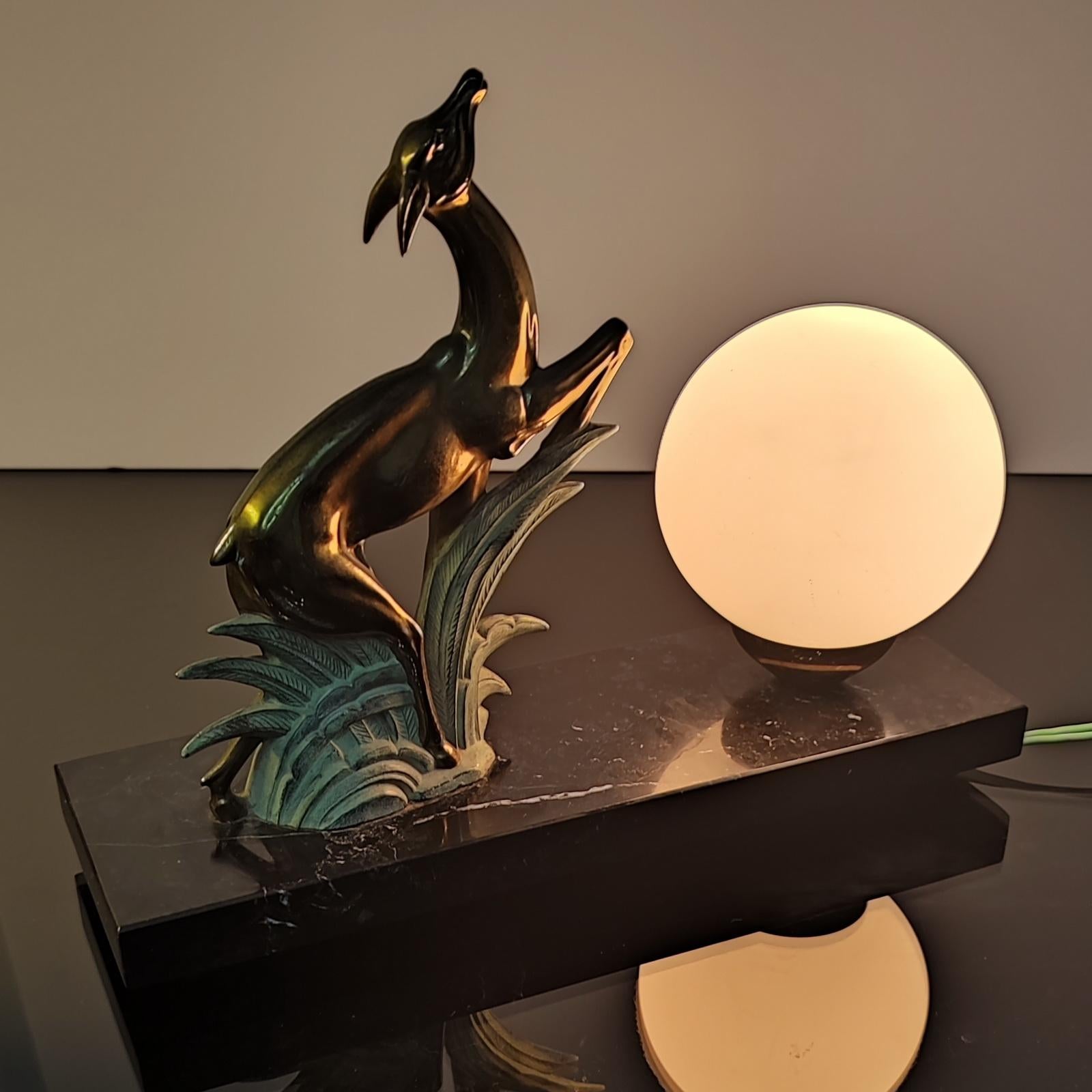 French Art Deco Antelope table lamp or night-light sculpture, 1930s. Jumping golden deer in green patinated spelter grass on its marble base. White glass globe shade (of the 1950s period). Illuminated by a bayonette bulb. 
A classic example of an