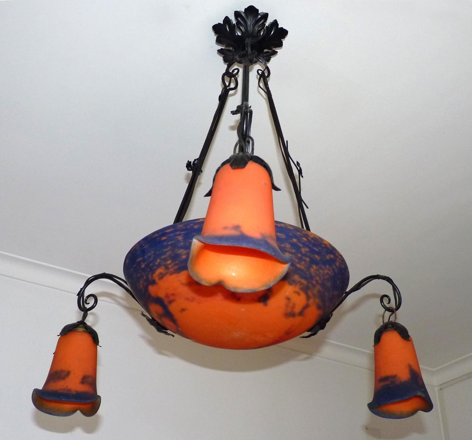 Beautiful original French signed 1930 Art Deco chandelier or pendant, signed Noverdy. It features a hand-forged wrought iron base with stylized leaf detailing and floral shaped glass shades in pate de verre glass, in hues of orange fire, blue,