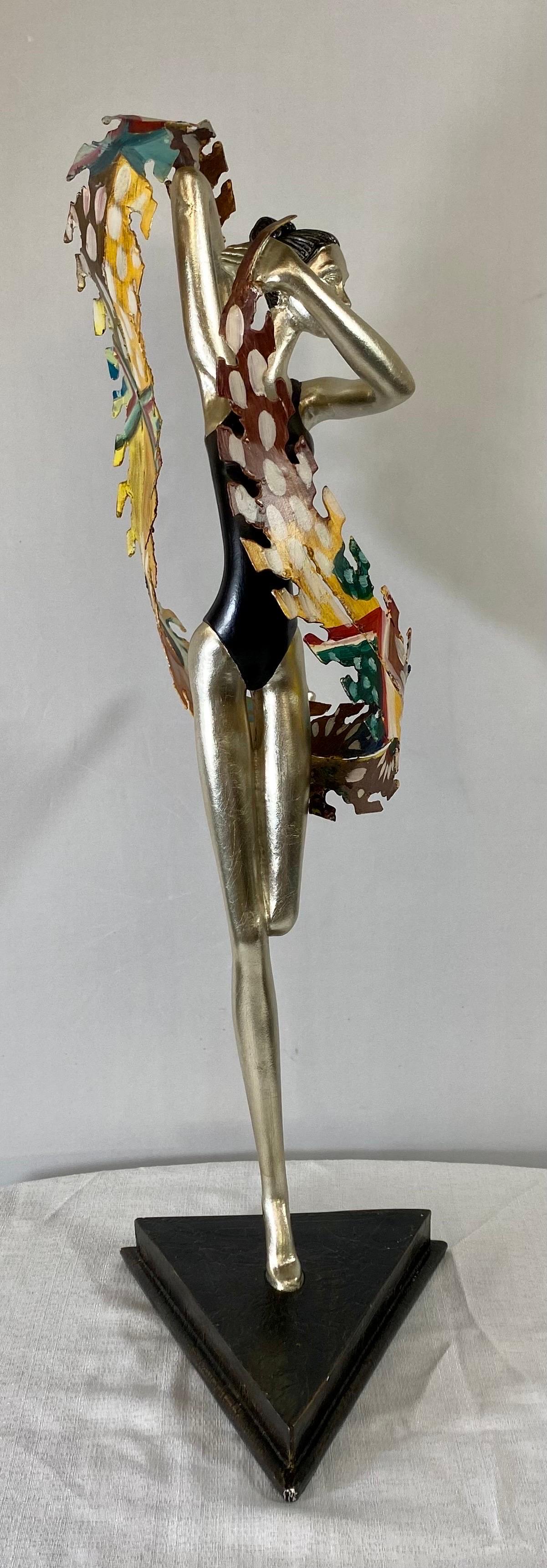 An elegant French Art Deco ballerina sculpture made of iron and resin. The sculpture depicts a dancing ballerina exuding grace and elegance through her lean body and dancing position. Holding a dancing scarf made of iron in multi-colors, the