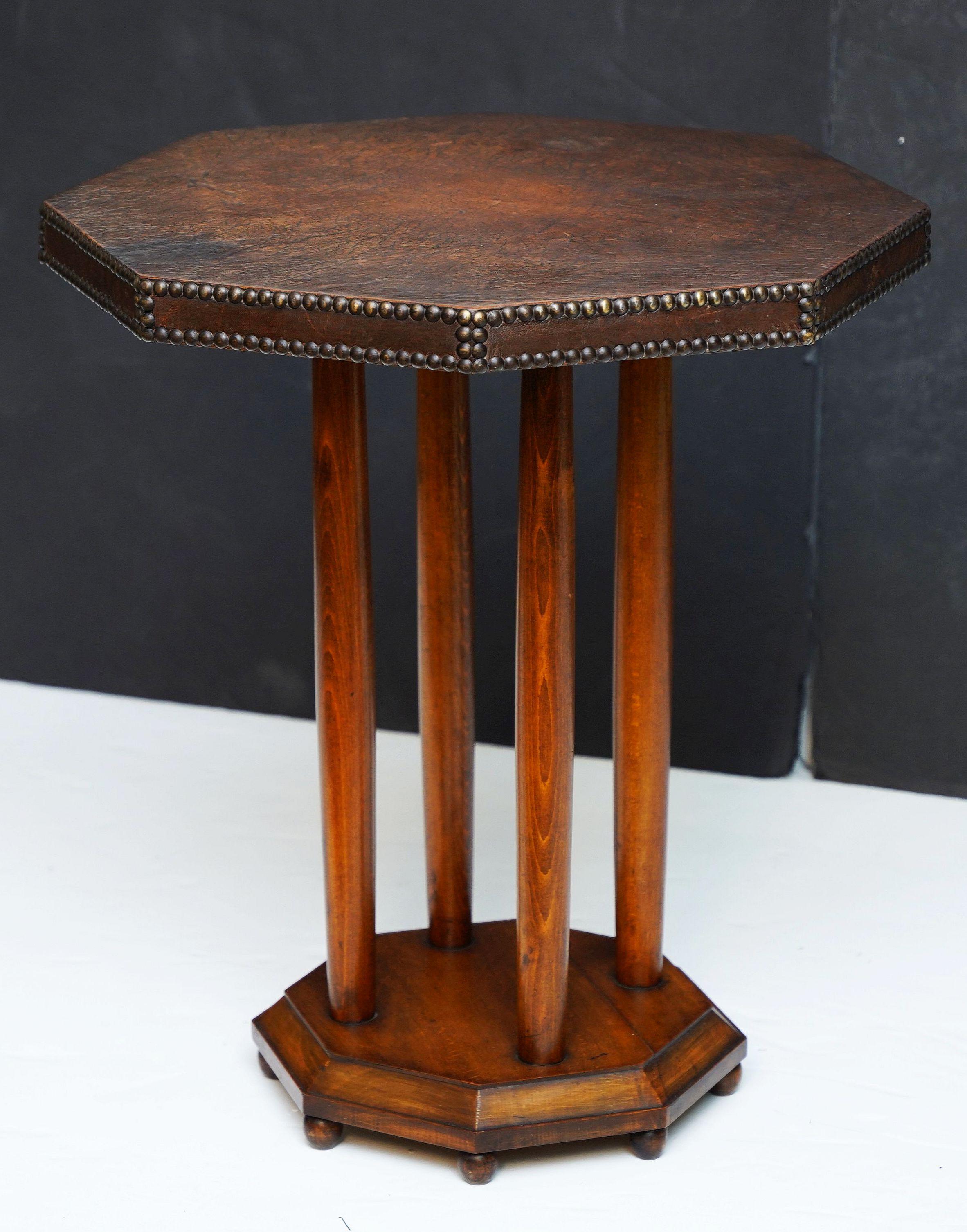 A fine French octagonal top occasional or bistro table from the Art Deco era, featuring a leather-wrapped top with brass nail-head detail, over four wood pedestal supports mounted to a smaller octagonal base, and resting on ball feet.

The leather