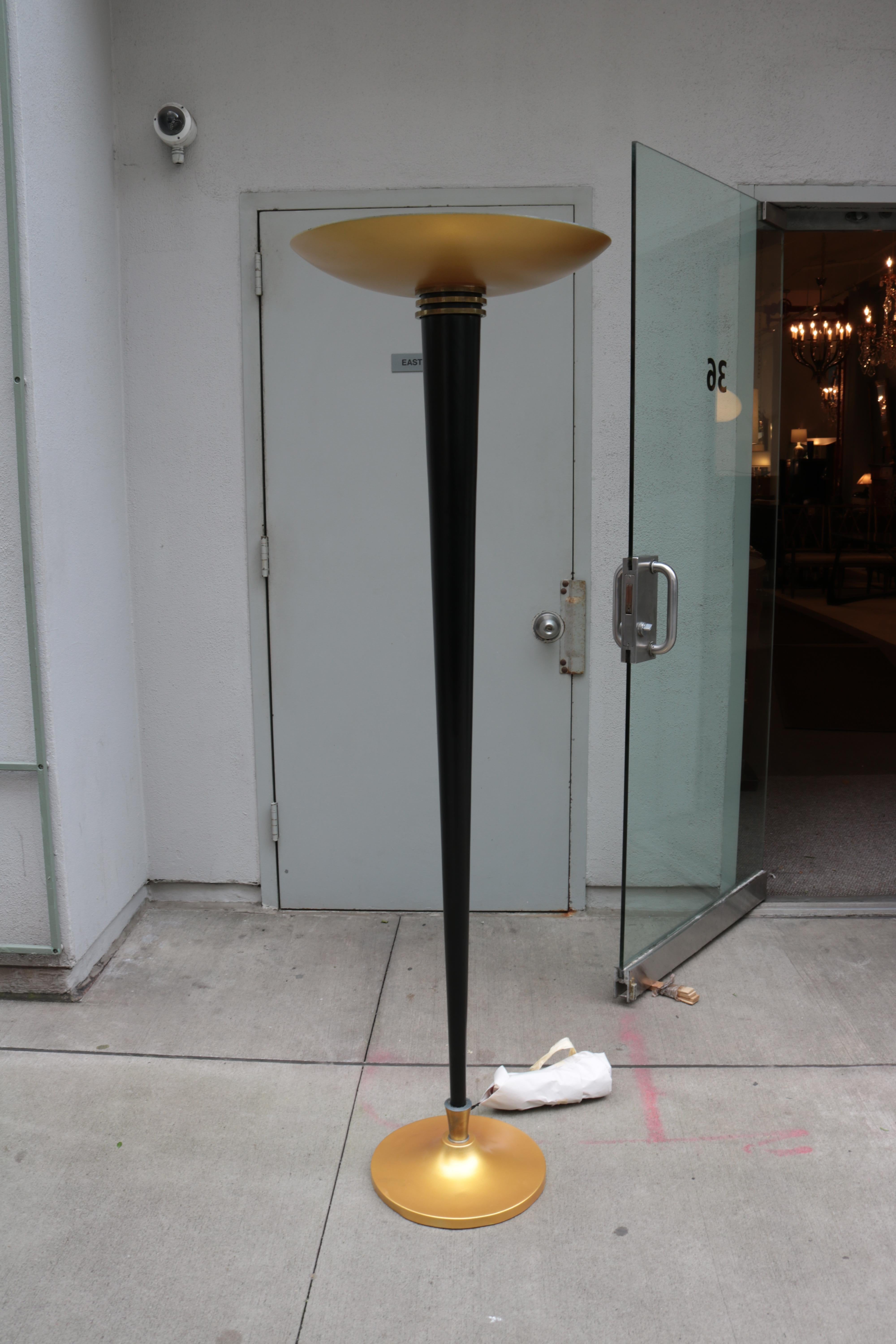 A French Art Deco period torchiere floor lamp from France circa 1930. The conical ebonized shaft stands upon a circular gold painted metal base and supports a shallow gold painted bowl concealing the light source.