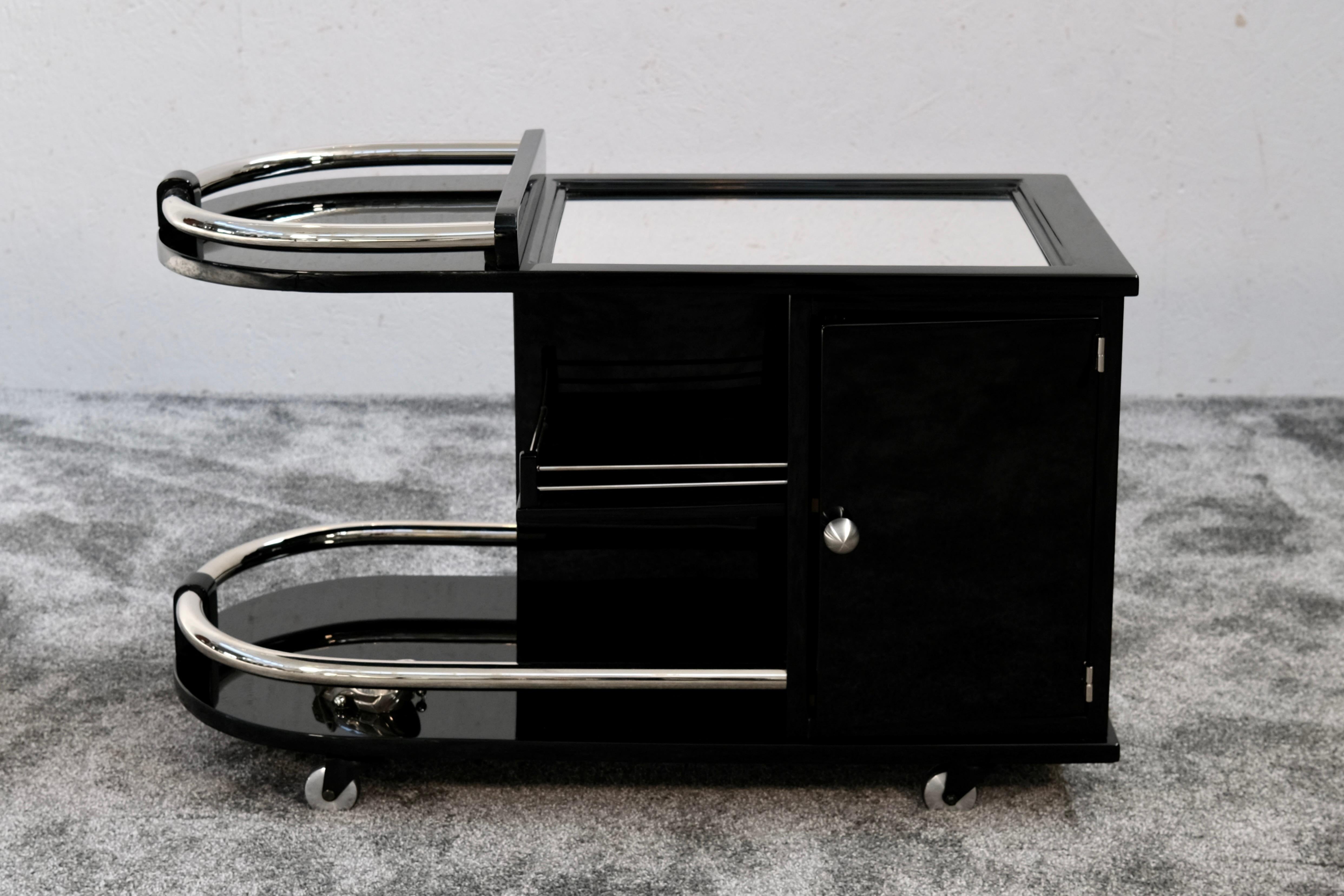 A French Art Deco bar cart in high-gloss black lacquer with chrome rails and mirrored glass top, crafted in France circa 1930. This original period piece embodies the streamlined sophistication of the Machine Age, combining functional design with